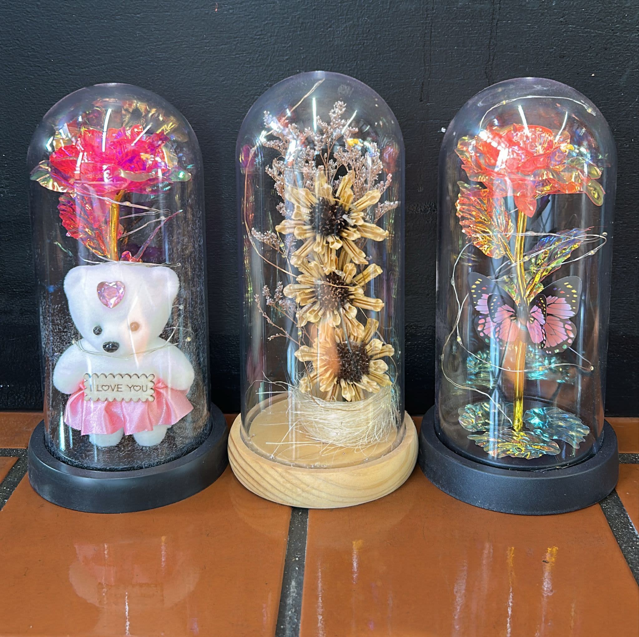 Three decorative dome displays with preserved flowers and a teddy bear.