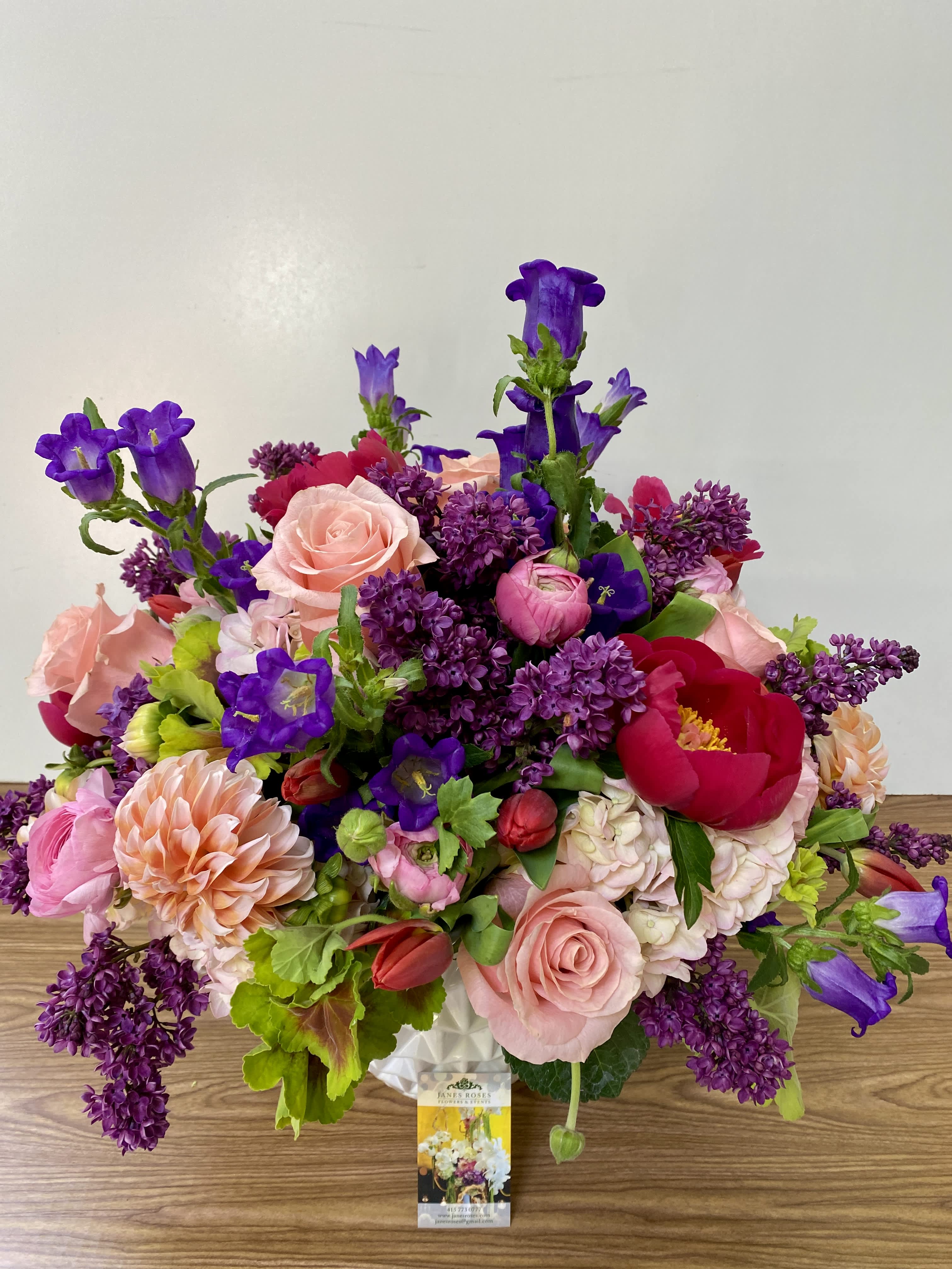 Mixed bouquet of pink, purple, and red flowers in a white vase