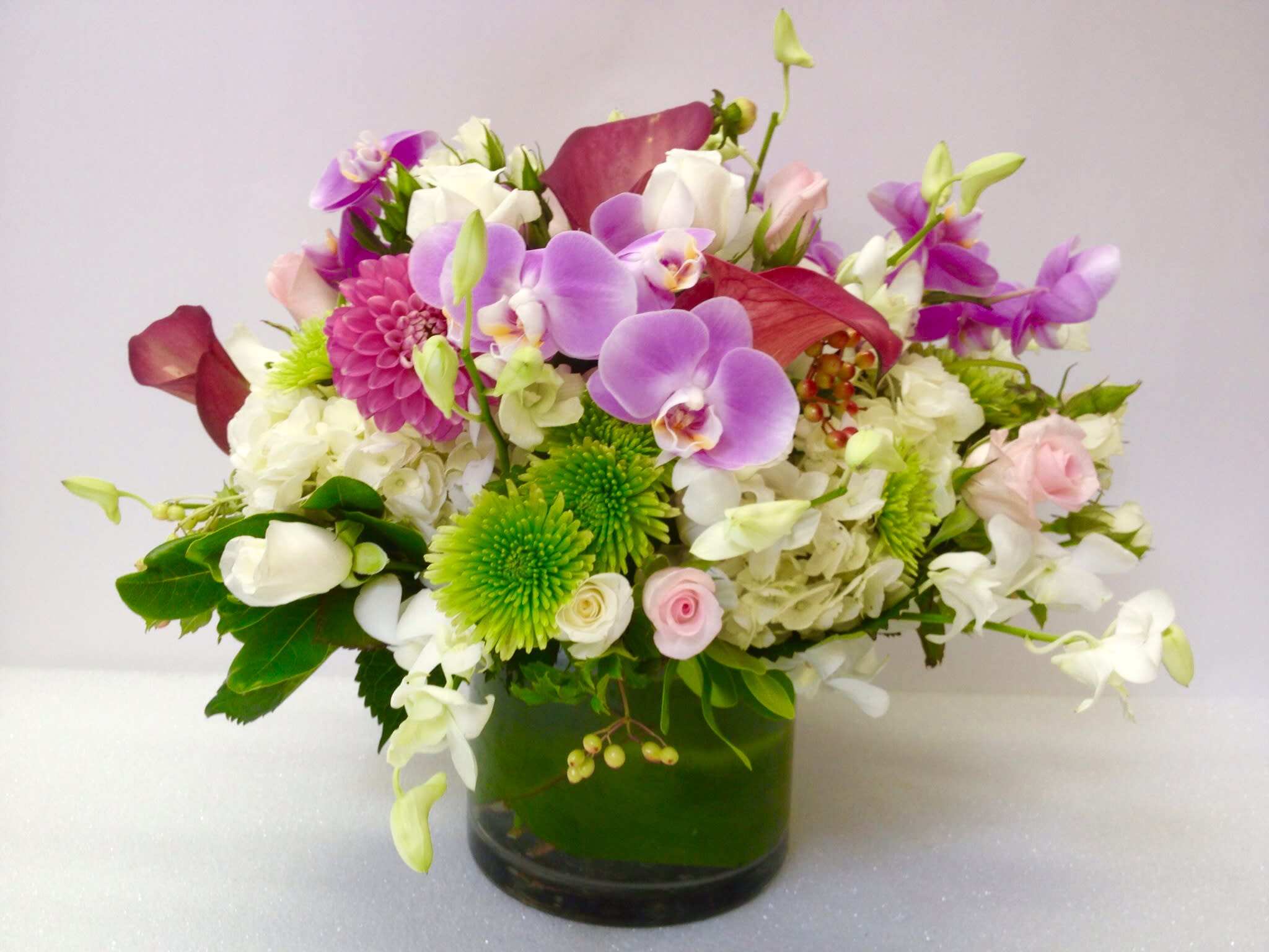 Mixed bouquet of orchids, roses, and chrysanthemums in a glass vase