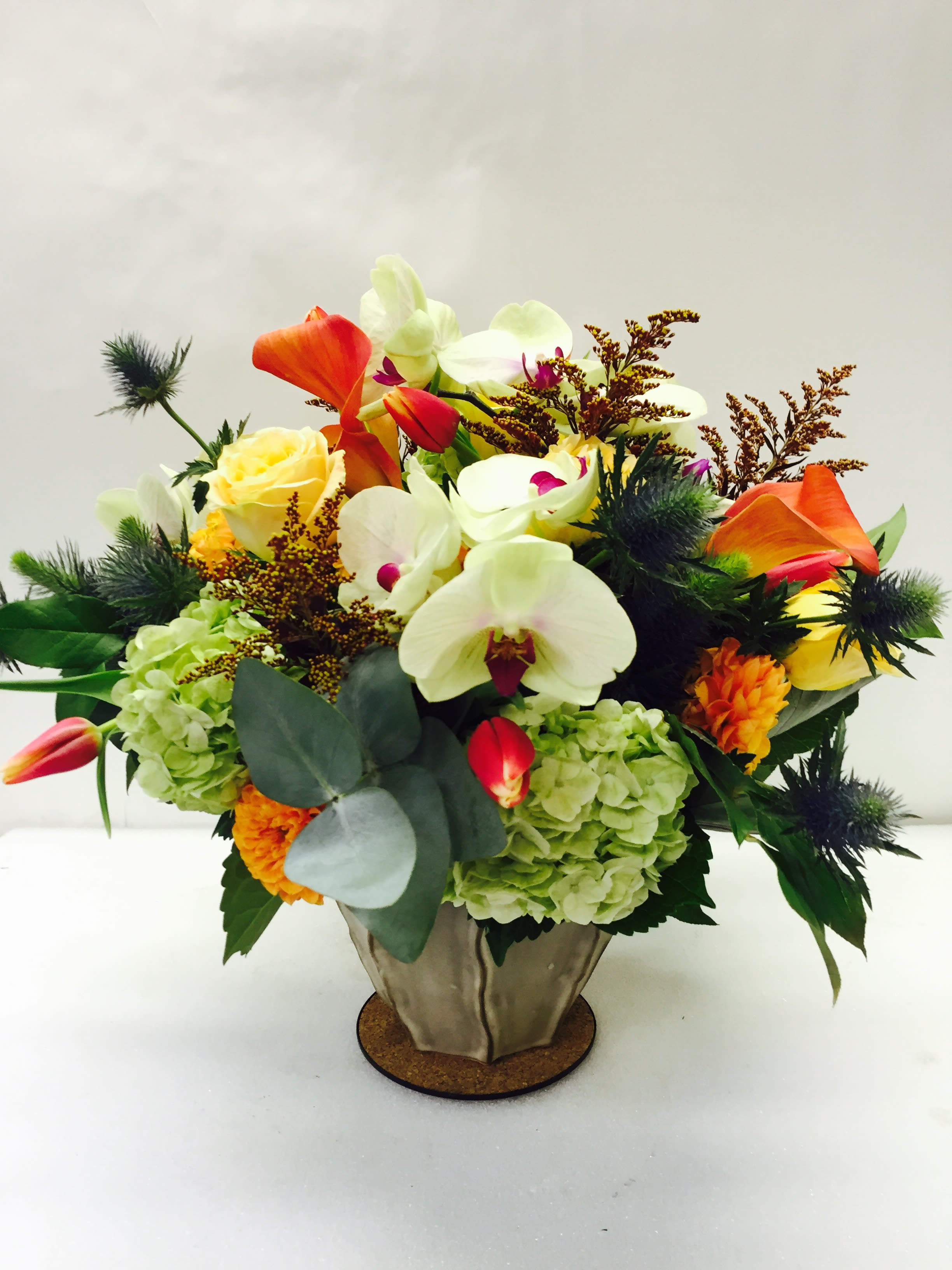 Mixed bouquet with orchids, roses, hydrangeas, and orange calla lilies in a metal vase