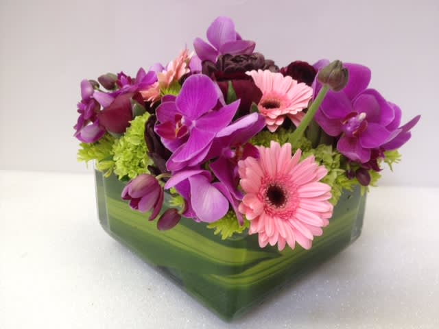 Pink gerbera daisies and purple orchids in a green glass vase