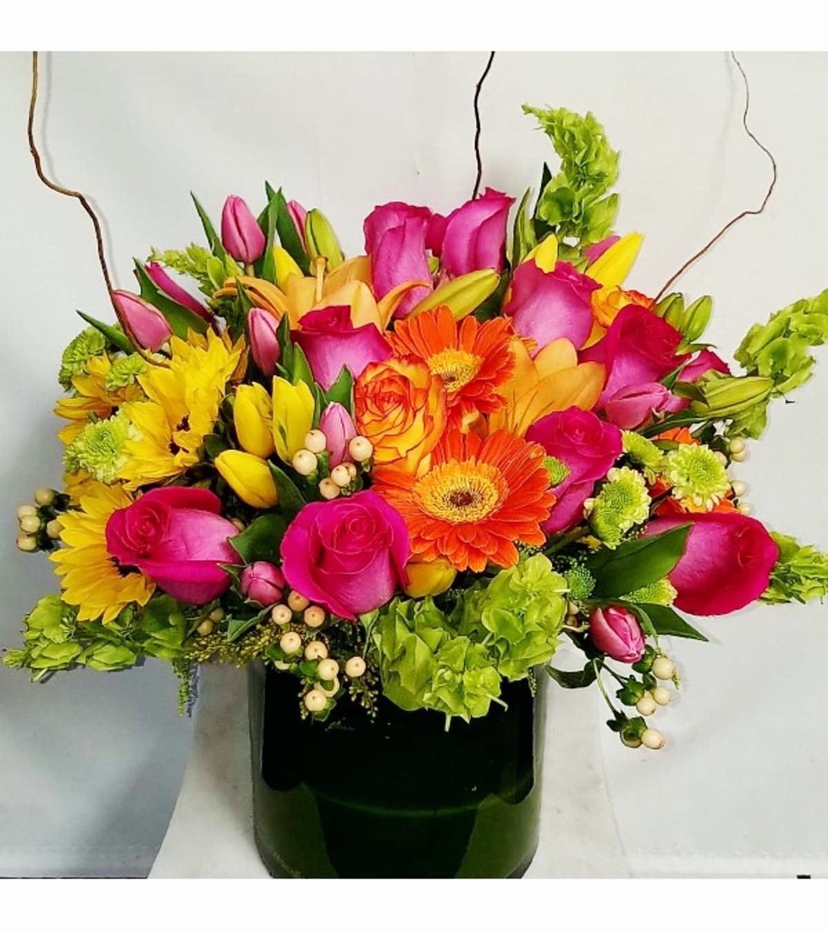 Bright mixed bouquet with pink roses, orange gerberas and yellow blooms in a dark green vase