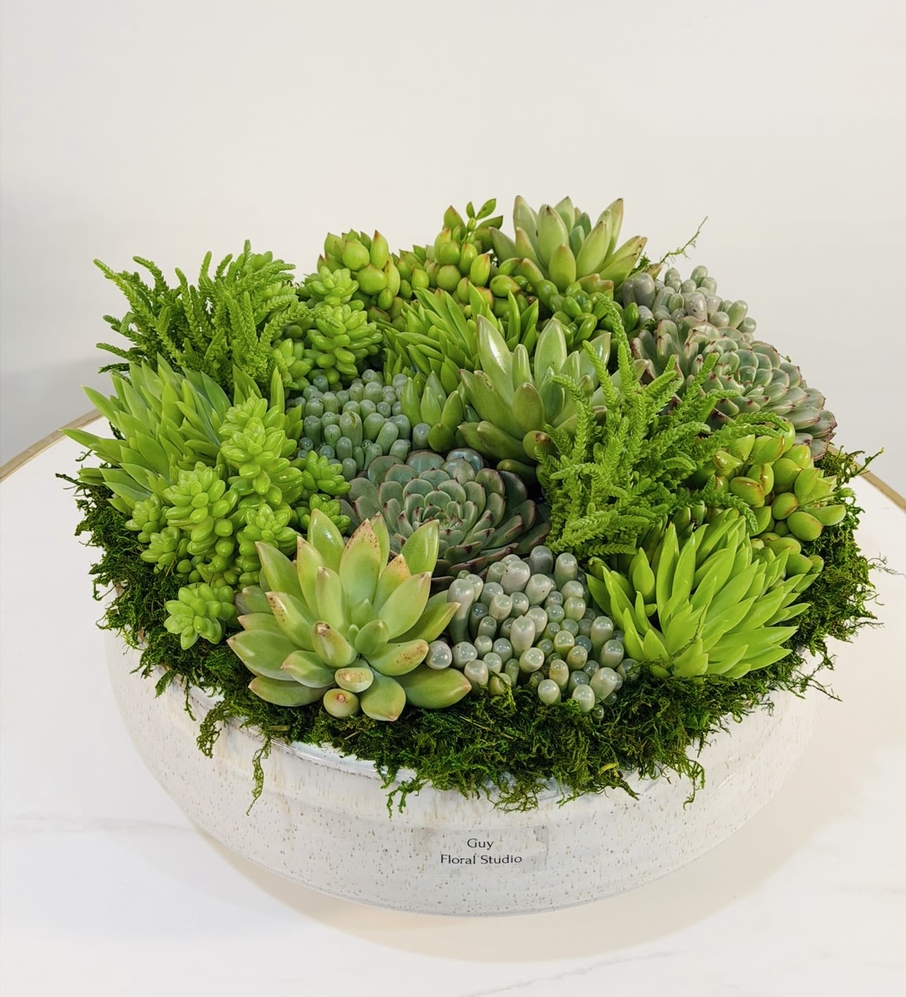 Luxury Succulent Garden Bowl - Elevate any space with this luxurious succulent garden bowl, exclusively designed by Guy Floral Studio. This stunning arrangement features a rich variety of premium succulents, carefully selected for their unique textures, vibrant green tones, and sculptural beauty. Set in a high end ceramic container, this design creates a full, lush, and modern look that makes a statement in any home, office, or event setting. Each succulent is thoughtfully arranged to achieve balance, depth, and a natural flow bringing a sense of calm and sophistication to the environment. Succulents are known for their durability and low maintenance, making this arrangement an excellent choice for gifts such as birthdays, corporate occasions, housewarmings, or luxury decor. This is a long lasting alternative to traditional floral arrangements while still delivering a high end aesthetic. Guy Floral Studio proudly offers same day delivery in Los Angeles, including Beverly Hills, Bel Air, West Hollywood, Hollywood Hills, Beverly Grove, Culver City, and Santa Monica. Every arrangement is handcrafted and delivered with care to ensure freshness and premium presentation. Product Dimensions: Height: 8 inches Width: 14 inches  Order today from Guy Floral Studio and enjoy modern luxury with reliable same day delivery.