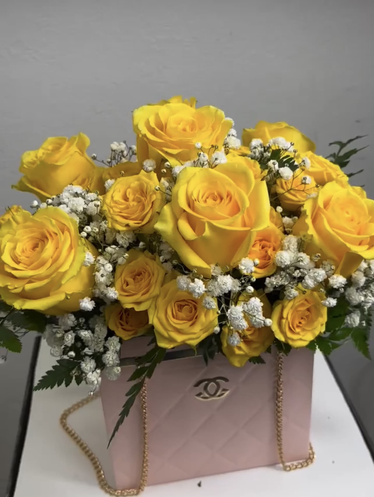 Yellow roses arranged in a pink gift box with baby's breath