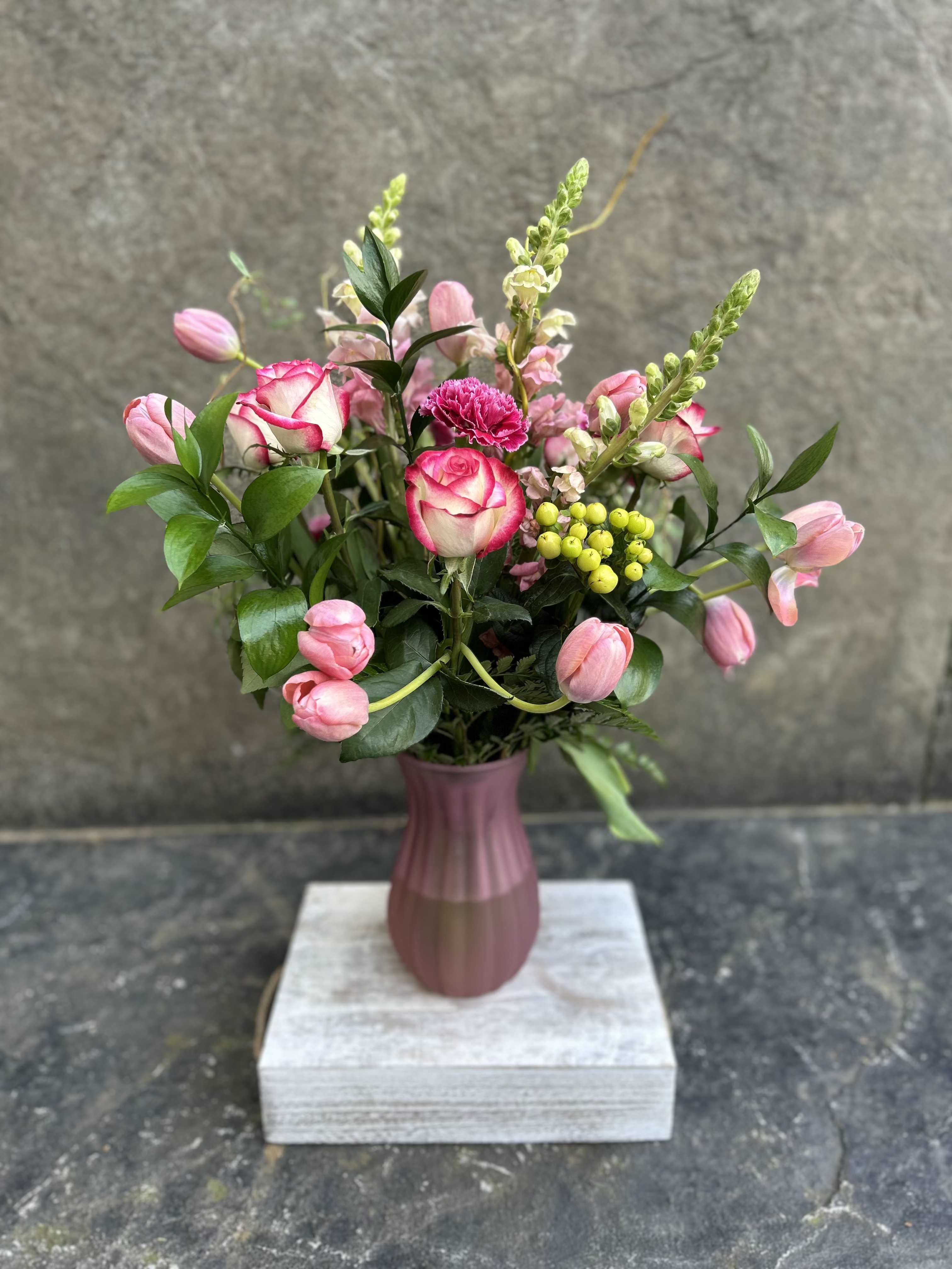 Raspberry Ice - Bi-color roses, tulips, carnations, berries , snap dragons, curly willow. a mix of greens in a tall matte pink textured vase! Color combo of pink and green! one of our faves that just makes us smile when we see it!   *Reasonable substitutions may be made due to floral availability. Will have similar look and feel.