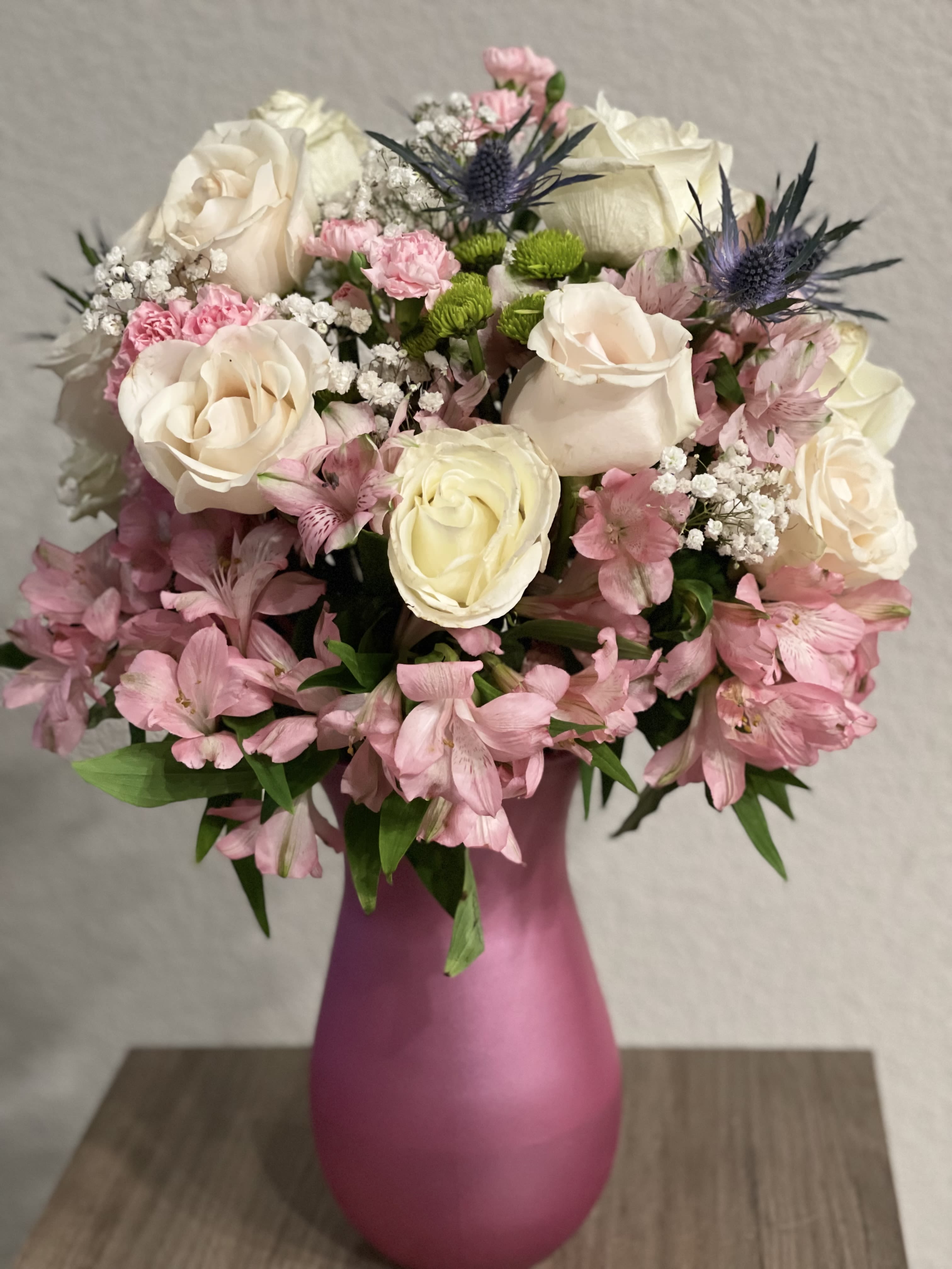 Polished Pearl - Lovely floral arrangement of long stem white roses, pink alstroemerias, baby’s breath flowers, assorted flowers and leather leaves all around on a tall pink vase.