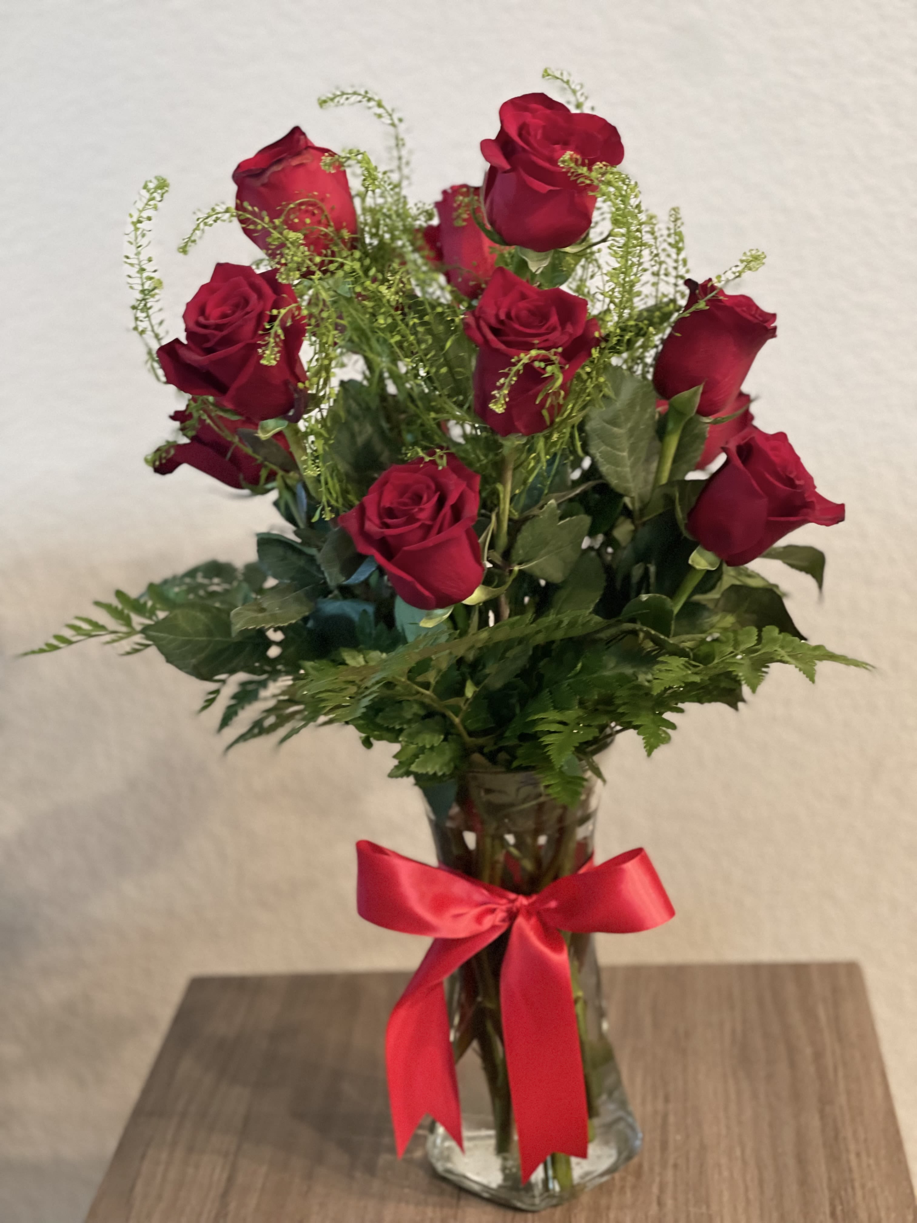 Red roses in a clear glass vase with a red ribbon