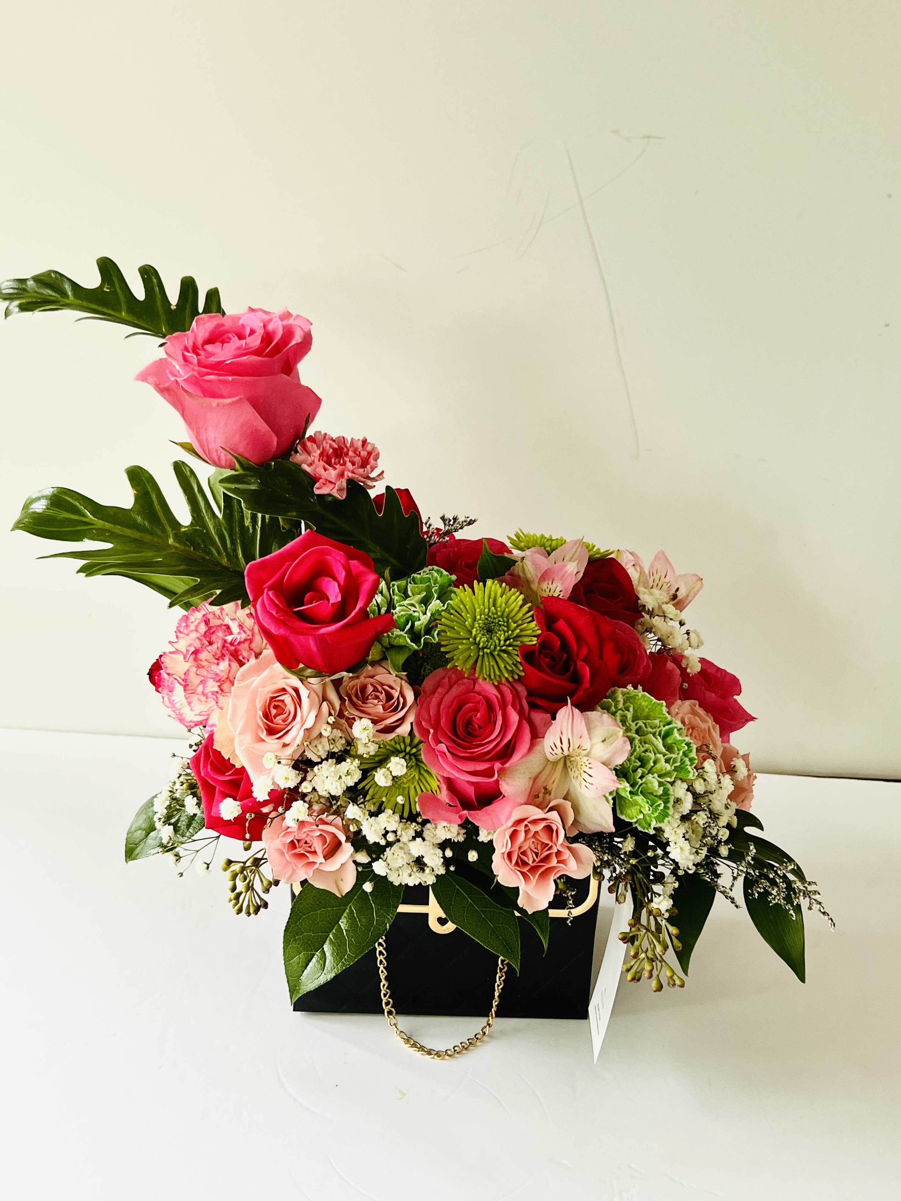 Pretty in Pink for Mom - A heartfelt Mother’s Day arrangement featuring a lush blend of pink and red roses, accented with soft carnations, delicate alstroemeria, and cheerful chrysanthemums—beautifully presented in a chic black handbag box as a timeless expression of love and appreciation.  