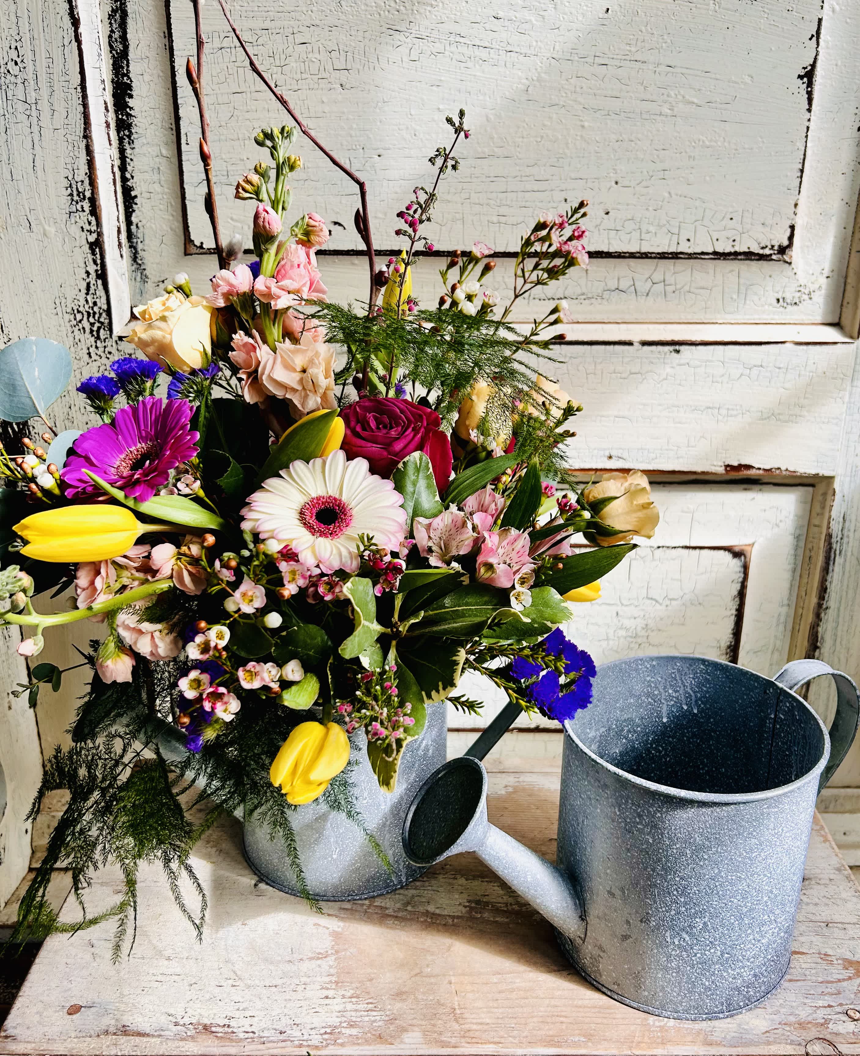 Mixed bouquet in a metal watering can with pink, yellow, white, and purple flowers
