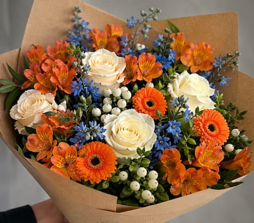 Syracuse Celebration Bouquet - Celebrate your graduate with our vibrant Syracuse Graduation Bouquet, designed in classic orange and blue tones to honor Syracuse University. This hand-tied bouquet features fresh orange alstroemeria, bright mini gerbera daisies, elegant white roses, white hypericum berries, and seasonal blue accent flowers, all wrapped in natural kraft paper for a modern, photo-ready look.  Perfect for Syracuse University graduation ceremonies, this bouquet is lightweight, easy to carry, and ideal for photos on campus, at the Dome, or around downtown Syracuse. Whether you’re celebrating a senior, gifting flowers to a proud parent, or surprising your graduate after the ceremony, this bouquet makes a bold and joyful statement.  Conveniently located near Syracuse University and local hotels, we offer easy graduation flower pickup in Syracuse, NY, making it simple for visiting families to grab a last-minute gift.   Why customers love this bouquet:  Designed in Syracuse University-inspired colors Perfect for graduation photos and celebrations Wrapped and ready for quick pickup Fresh, seasonal flowers arranged in a modern style  Pre-order your Syracuse graduation flowers today to ensure availability during one of the busiest weekends of the year.