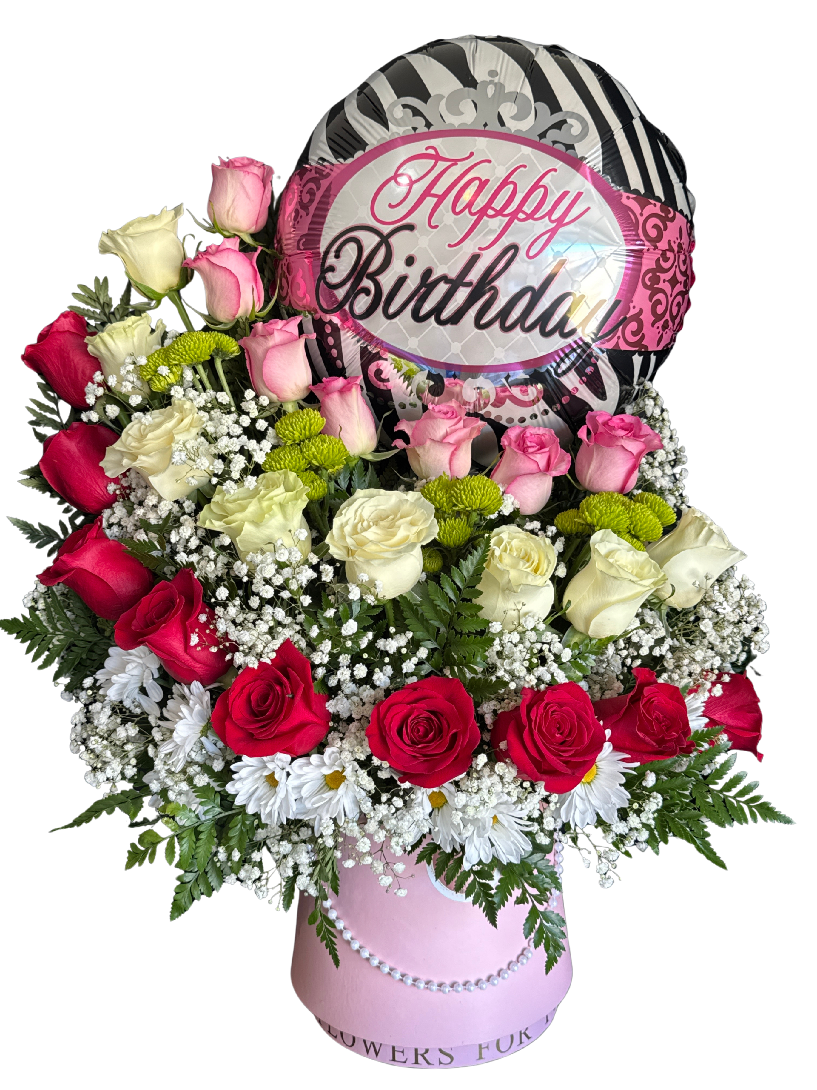 Queen of roses - Velvety pink, red, and ivory roses mingle with cheerful white daisy-like blooms in a soft, feminine birthday arrangement that feels both romantic and celebratory. This flower arrangement for birthday gifting places the recipient front and center-she'll feel adored and celebrated the moment the pink foil balloon that reads "Happy Birthday" floats above the blossoms.  Tightly packed in a polished pink cylindrical hatbox with pearl trim, the Queen of roses pairs classic roses with small green chrysanthemum accents for texture and freshness. The mix of roses, daisies, and chrysanthemums creates a lush, rounded silhouette and a pleasing contrast of smooth petals and spiky green centers.  Perfect for a daughter, sister, close friend, or special someone who loves a romantic palette, this hatbox arrangement arrives ready to display on a table or mantle-no vase needed. Order in time for the birthday; to keep blooms fresh place them in a cool spot away from direct sun and refresh the water below the foam as directed with any boxed arrangement.