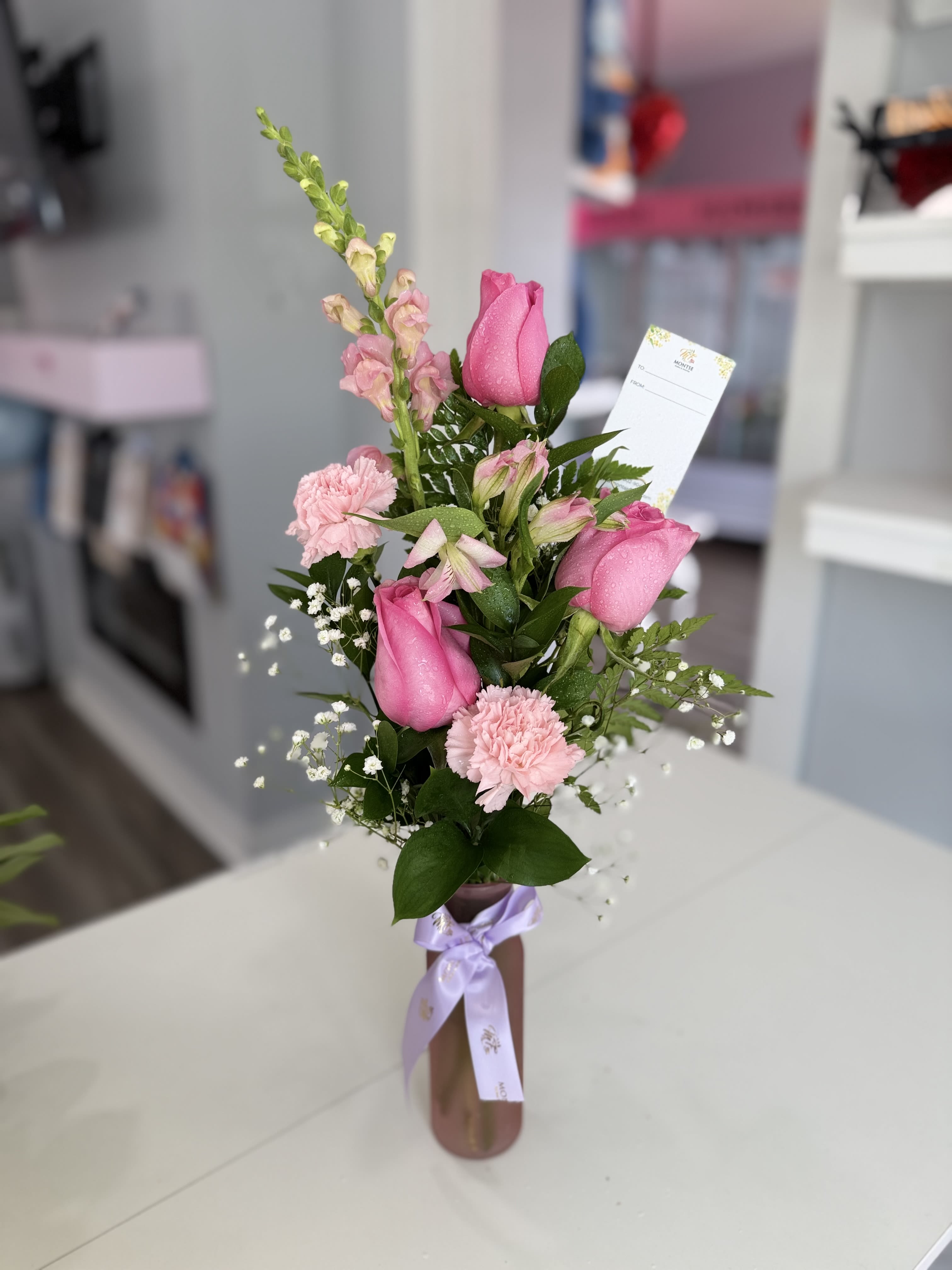 Marie  - Bright pink roses, pale carnations and snapdragons with greenery in a glass vase, lavender ribbon.