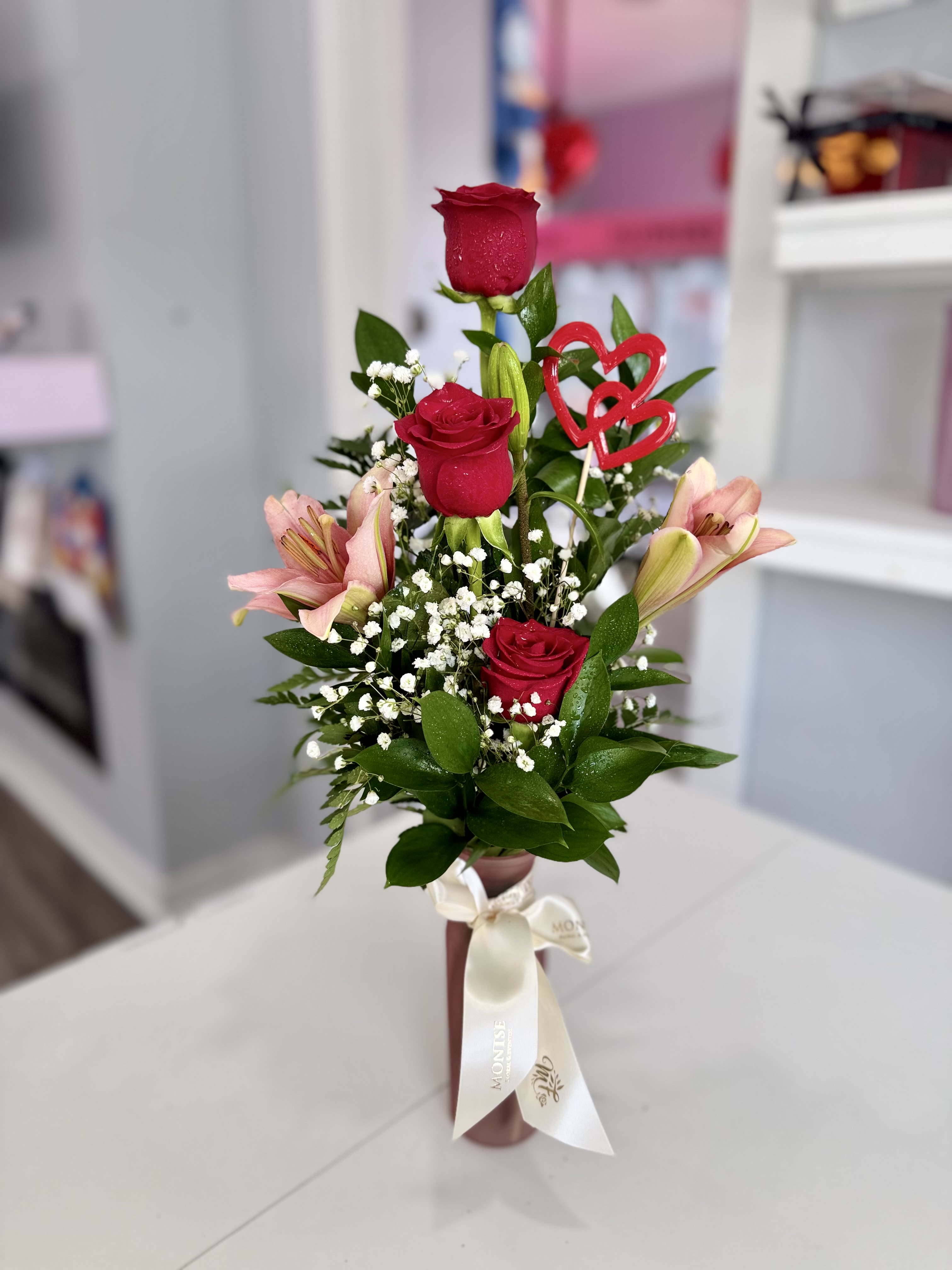 Thinking of you  - Three red roses with pink lilies, baby's breath and glossy greenery in a ribboned glass  vase with heart picks.
