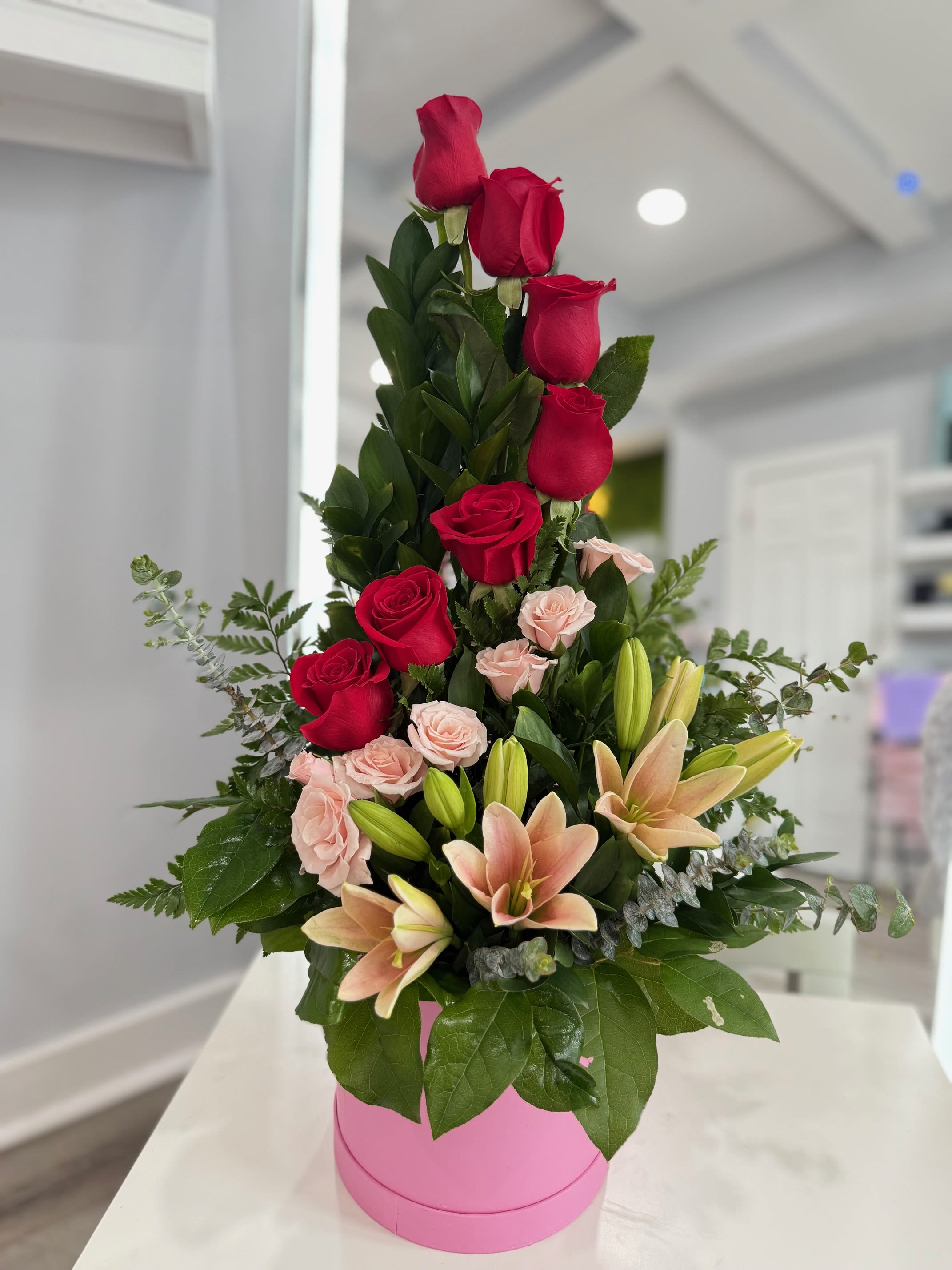 Sarah  - Tall arrangement of red, pink roses and lilies in a bright pink round box, structured and romantic