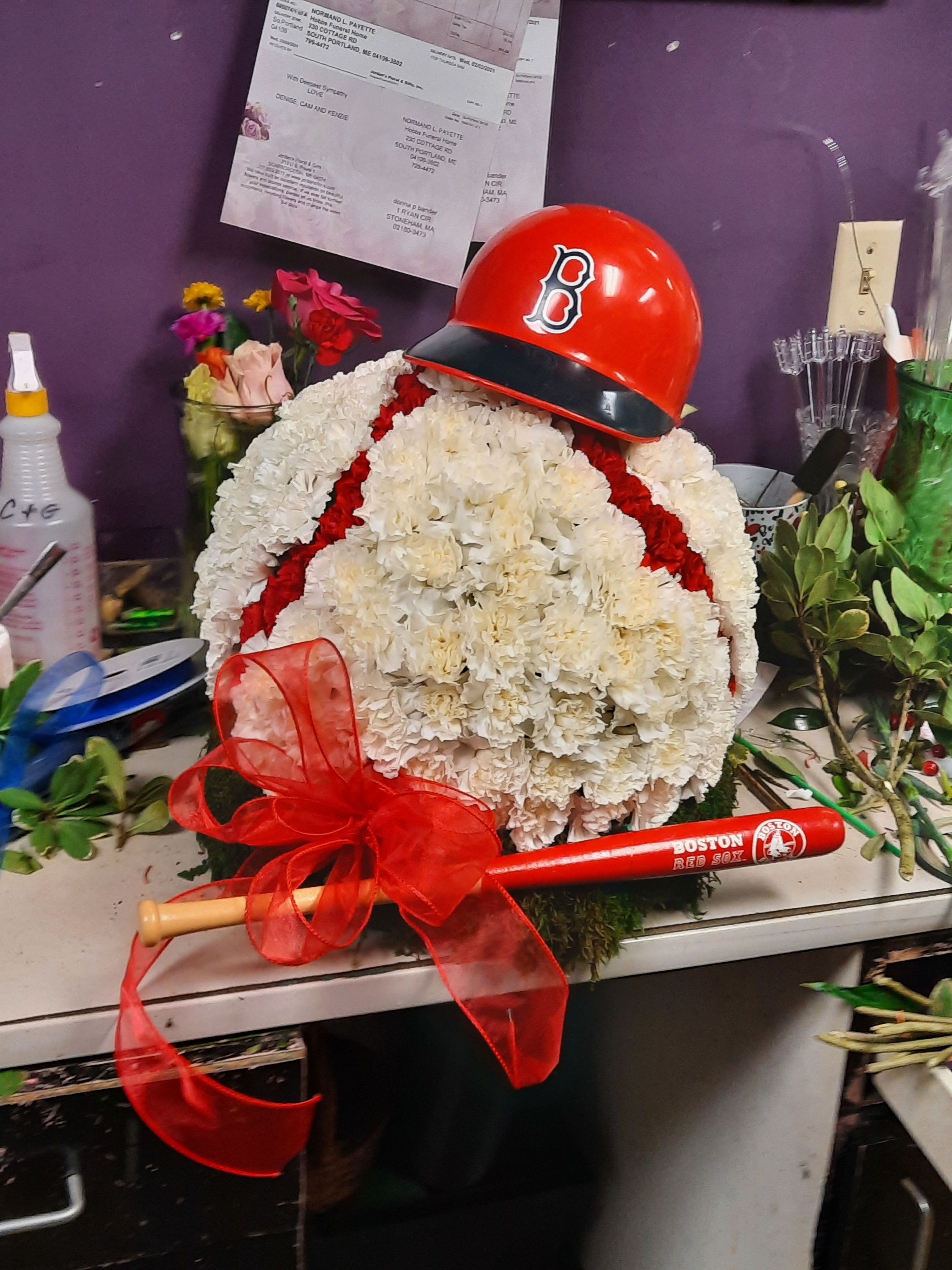 White floral arrangement with a red baseball helmet and bat