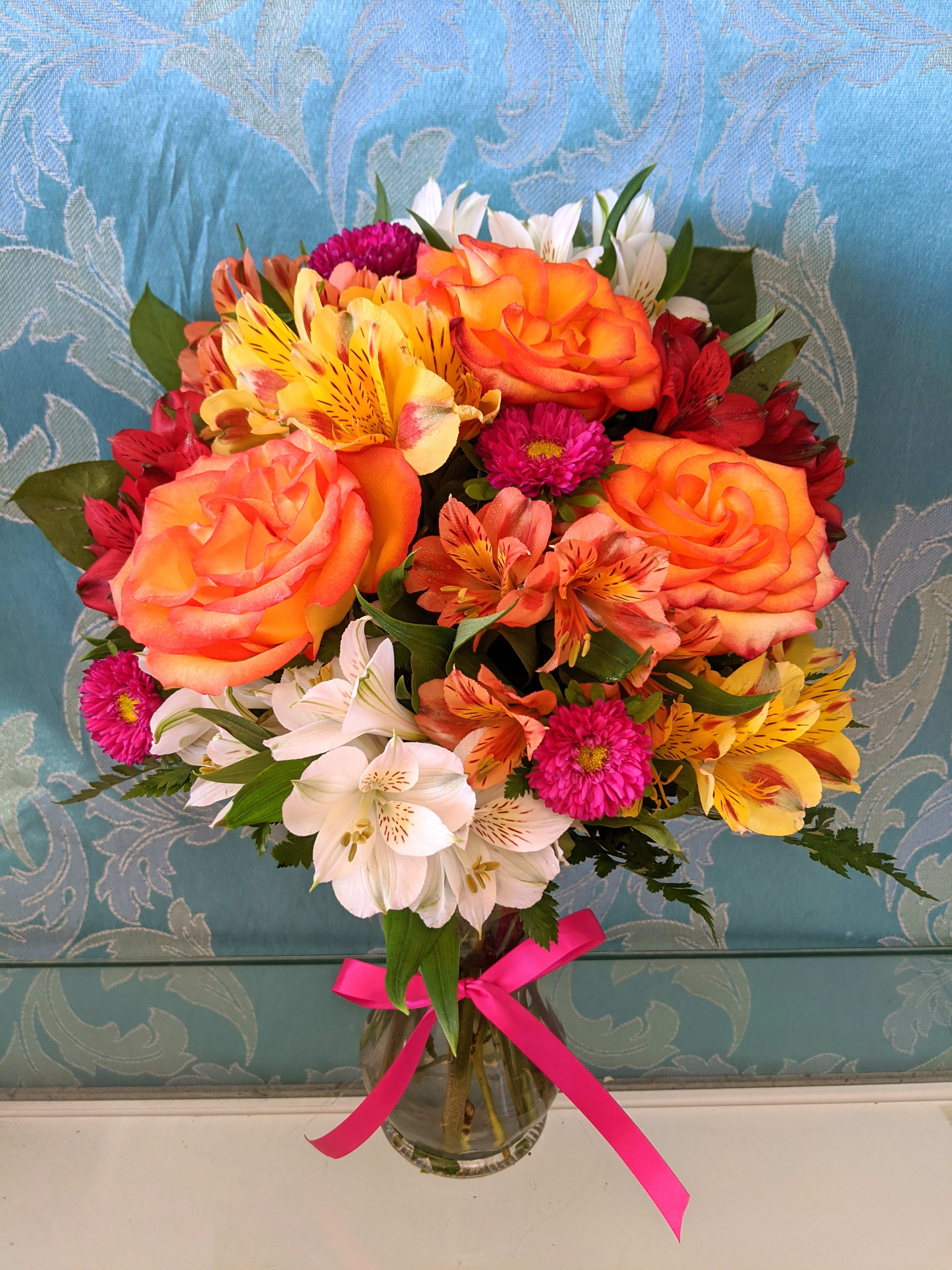 Mixed bouquet of orange roses, white lilies, and pink flowers in a glass vase