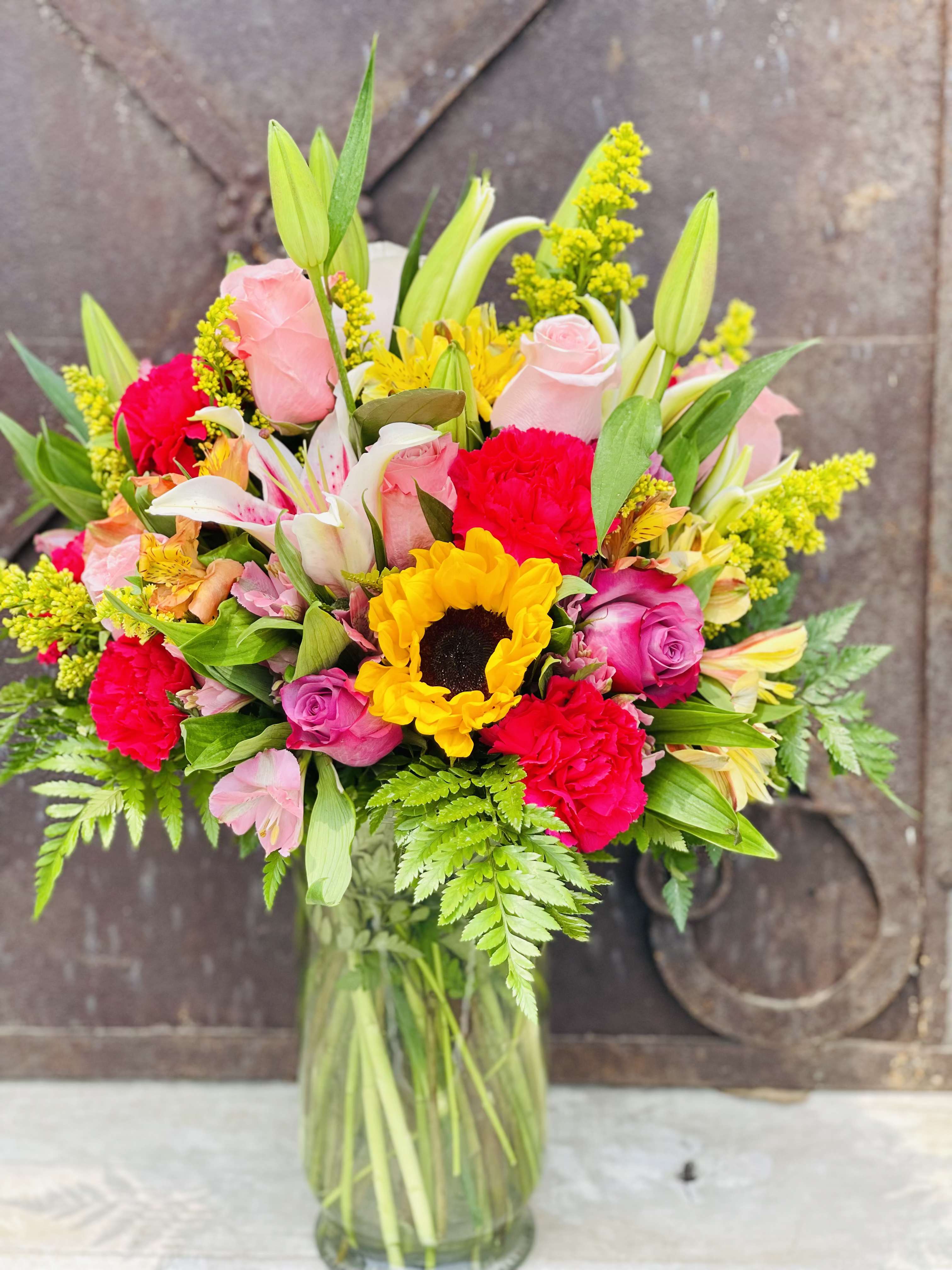 Mixed bouquet of roses, lilies, sunflowers, and carnations in a glass vase