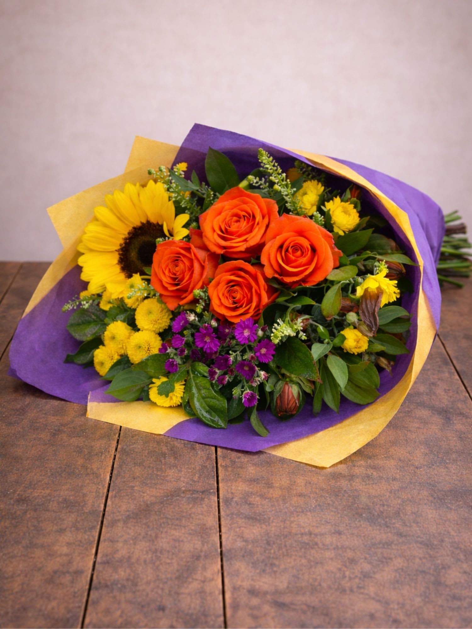 Bouquet of orange roses and a sunflower wrapped in purple and yellow paper