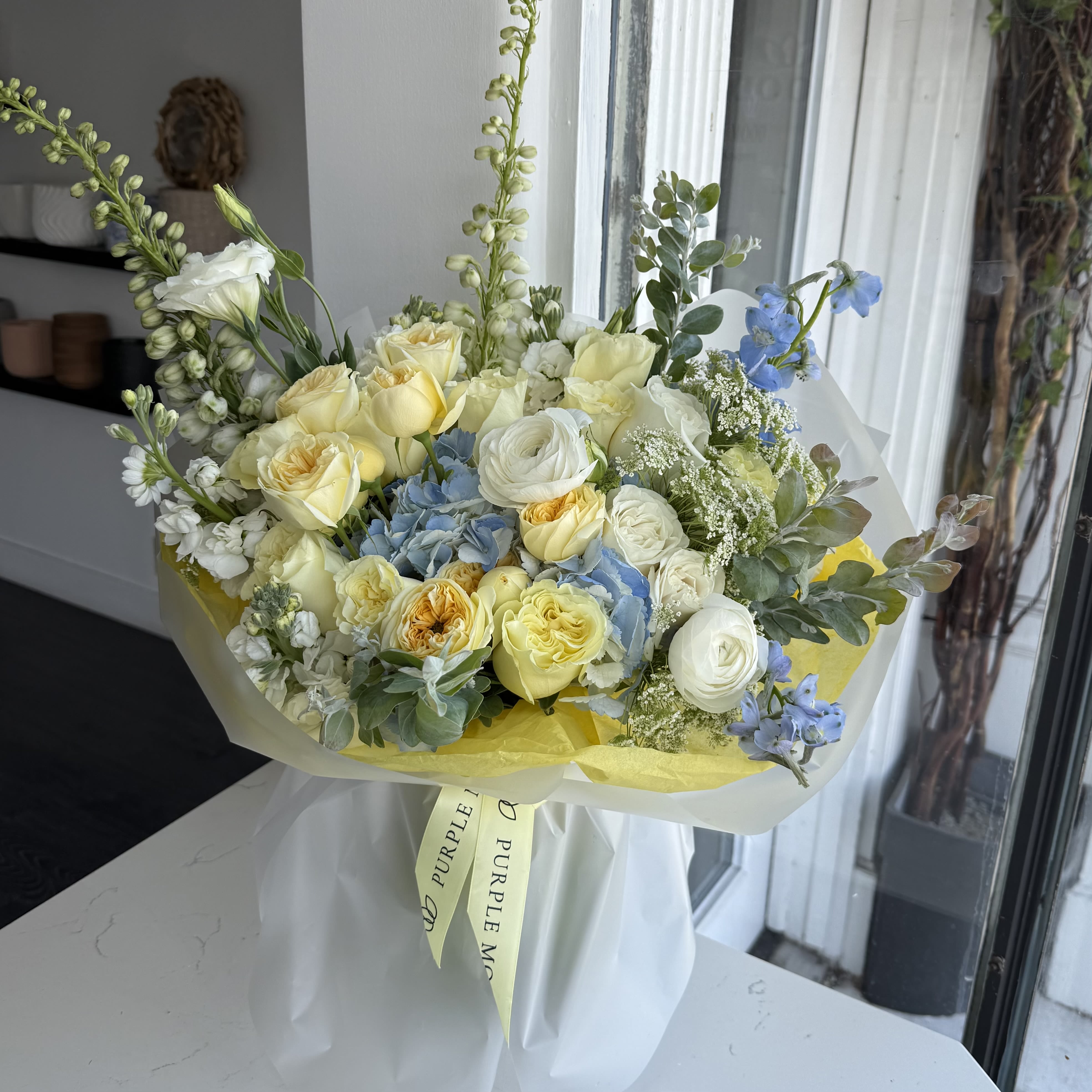 Sunny Bouquet - Sunny Bouquet Bright, cheerful, and full of warmth — the Sunny Bouquet is like a ray of sunshine brought indoors. Its mix of golden yellows, fresh whites, and soft blues creates a joyful harmony that instantly uplifts any room.      •    Wrapped in soft yellow accents for a glowing finish     •    A balanced and refreshing color palette     •    Available in Standard, Deluxe, and Premium sizes     •    Perfect for birthdays, thank-you gifts, or to brighten someone’s day  VASE NOT INCLUDED