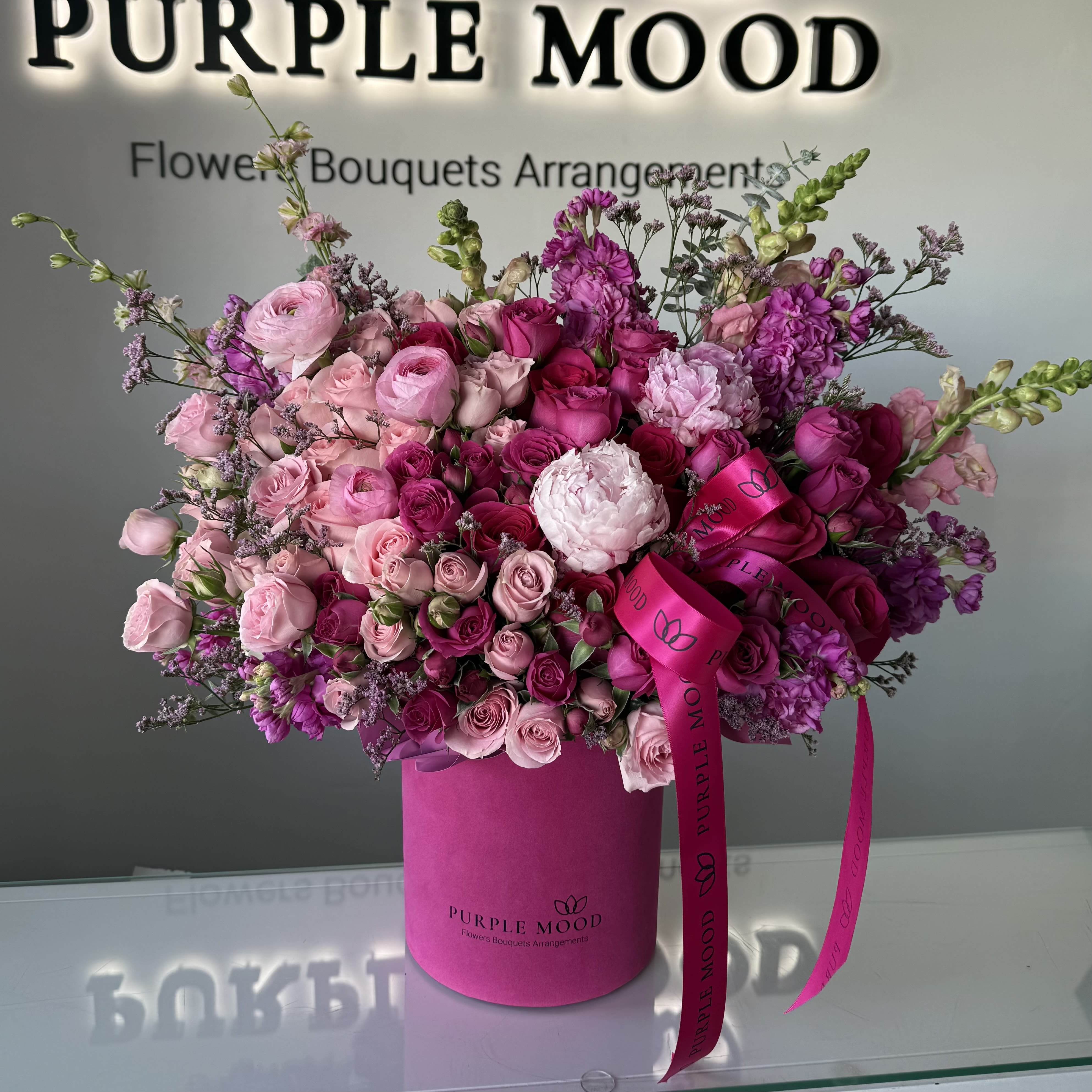 Large pink hatbox arrangement of pink roses, spray roses, peonies, and snapdragons with bright fuchsia ribbon.