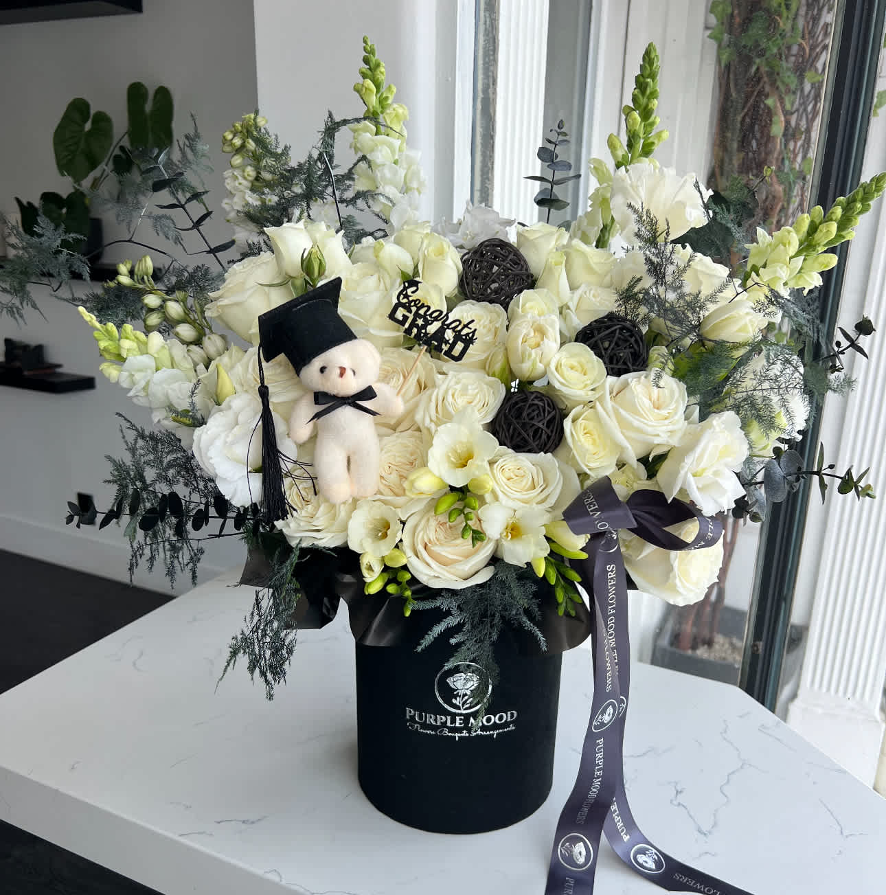 White rose bouquet in a black hatbox with a small teddy bear