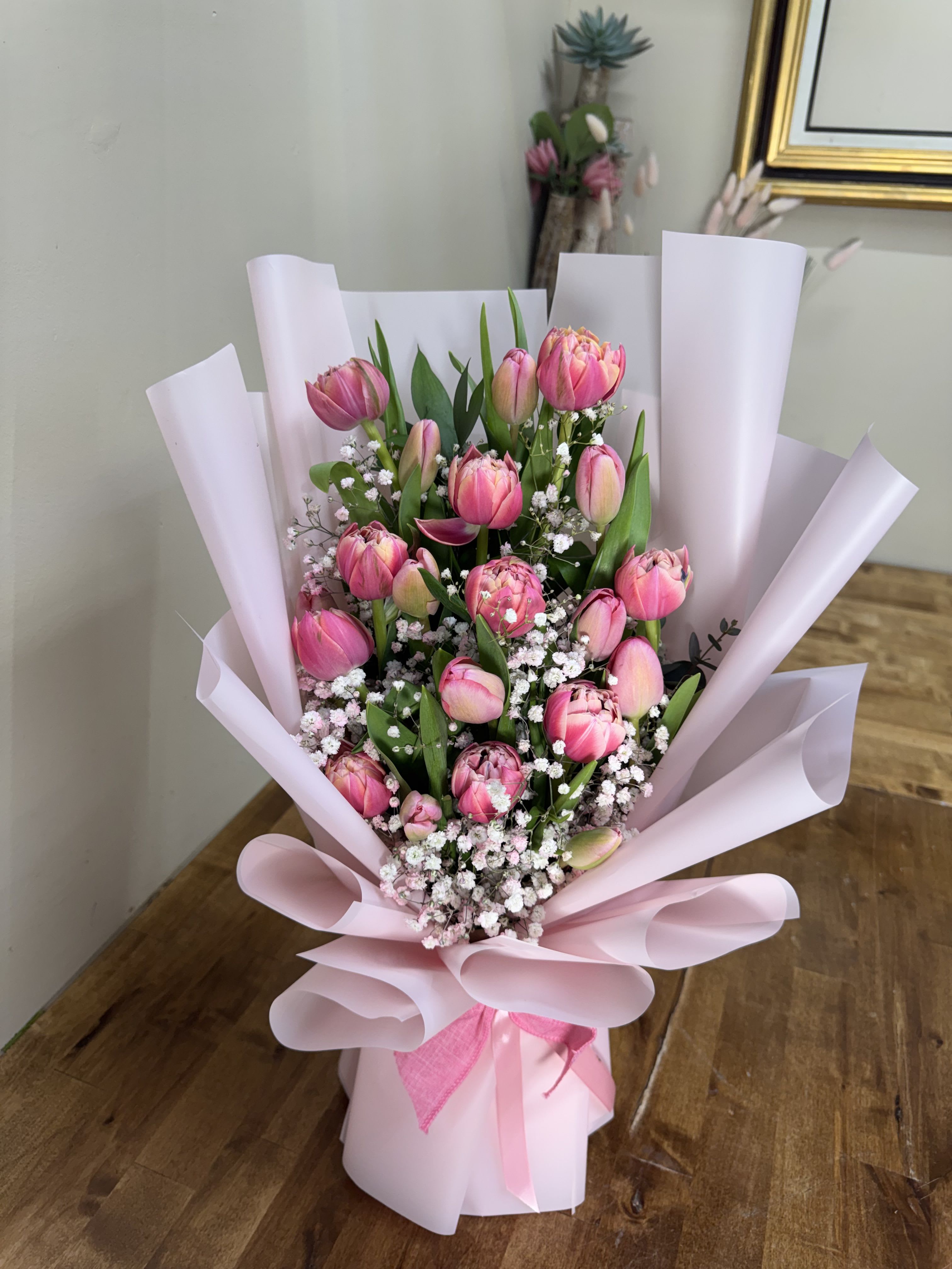 pink tulip dreams  - Soft pink tulips gathered in a garden-fresh cluster make this bouquet an ideal spring birthday bouquet, anniversary flowers, or romantic gesture. The mix of open and closed tulip blooms plus delicate white filler creates a textured, feminine look that reads as both thoughtful and effortlessly romantic-perfect for the person you want to make feel seen and adored.  Wrapped in large pale pink paper panels and tied with a matching pink ribbon, this hand-tied arrangement presents beautifully straight from the shop and is ready to gift. Colors are pink, white, and green; expect multiple tulips in varying stages of bloom with small white accents for contrast. Gentle care: keep stems in fresh water, trim stems at an angle every couple of days, and display away from direct heat to prolong blooms.