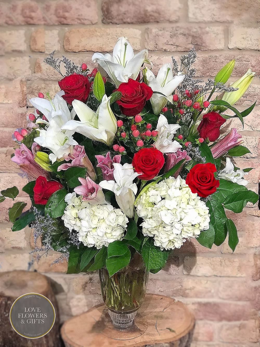 Tall bouquet of red roses, white and pink lilies, and white hydrangeas in a clear glass vase