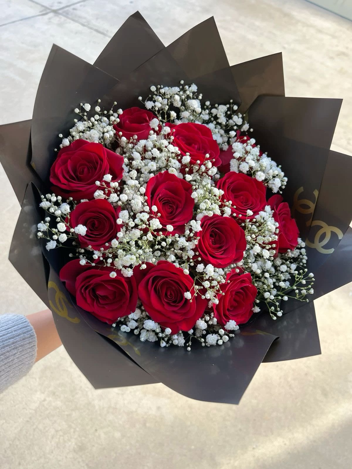 Handheld bouquet of red roses and white filler flowers wrapped in dark black paper
