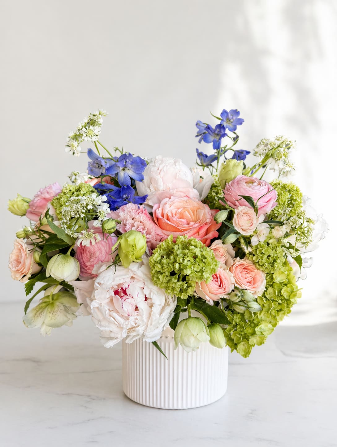 Pastel Dream Garden - Mother's Day Edition - A soft, elegant Mother’s Day arrangement in blush pink, creamy white, and refined pastel tones—artfully designed to capture the beauty of a blooming spring garden. Approximate size: 12"–14"W x 10"–12"H Flower selection may vary based on seasonal availability while maintaining overall color palette and style.