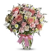 Cotton Candy - Soft blush and creamy white roses mingle with petite daisy-like blooms and airy filler to create a Cotton Candy flower arrangement ideal for a birthday, anniversary, or a heartfelt just-because surprise. The rounded, garden-fresh silhouette and whispery touches of muted purple and pale green give the bouquet a tender, feminine feel that will make the person you're thinking of feel genuinely celebrated and seen.  Arranged in a clear glass vase and finished with a wide pink ribbon, this compact display balances polished presentation with a gentle, everyday charm. Expect a harmonious mix of pink and cream roses, white accents, small daisy-style flowers, and light greenery-an arrangement that reads soft, romantic, and cheerful from every angle.  Perfect for spring occasions, thank-yous, or to brighten someone's day, Cotton Candy arrives gift-ready in the tied glass vase so no fussing is required. Light floral care-fresh water and a cool spot away from direct sun-will help the bouquet stay lovely for days.