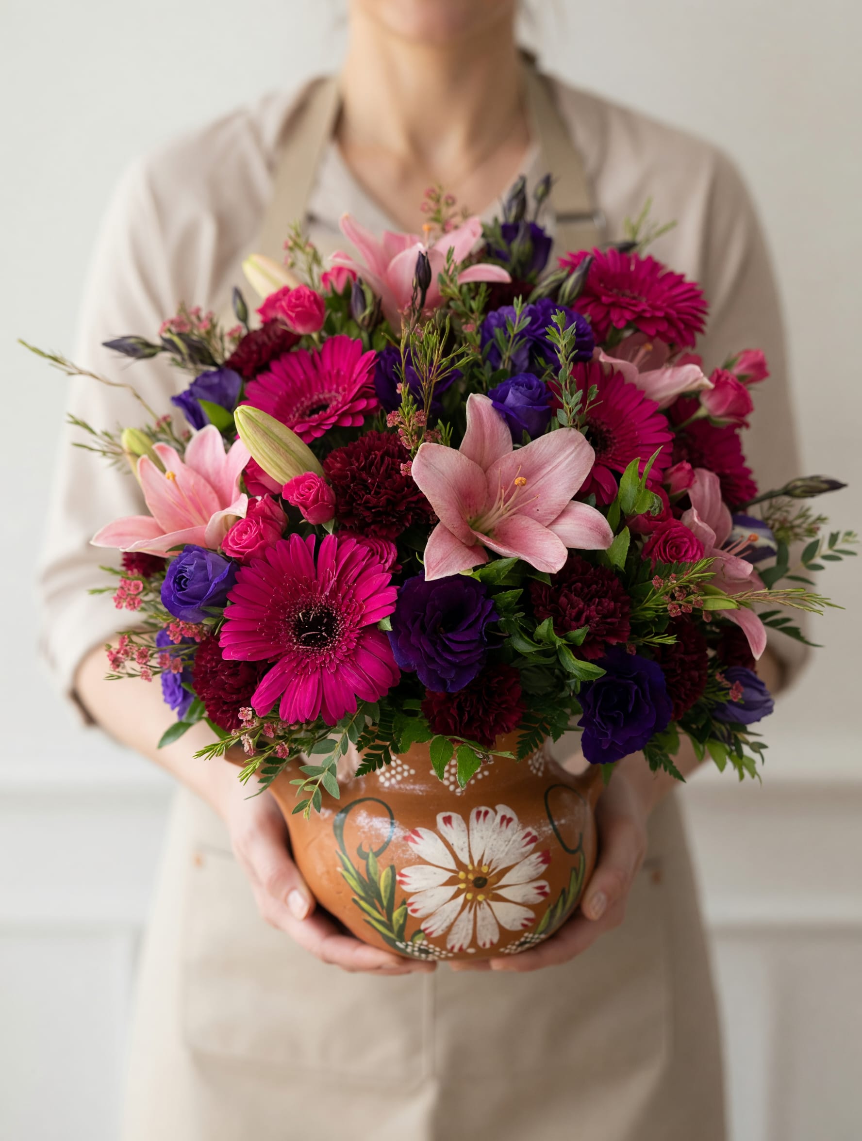 Amorosa Cayetana  - Celebra a mamá con un detalle lleno de vida, color y elegancia. Este hermoso arreglo floral combina delicadamente gerberas en tonos fucsia vibrante, lirios rosados, rosas miniatura y acentos en tonos profundos morados, creando una composición armoniosa que transmite amor, gratitud y admiración. Diseñado en una encantadora base de cerámica artesanal con detalles florales pintados a mano, este arreglo no solo destaca por sus flores frescas, sino también por su presentación cálida y auténtica que lo convierte en un regalo memorable. Cada pieza es elaborada cuidadosamente para reflejar la belleza y fortaleza de mamá, haciendo de este arreglo el regalo perfecto para sorprenderla en su día especial. Haz de este Día de las Madres un momento inolvidable con flores que hablan desde el corazón.   