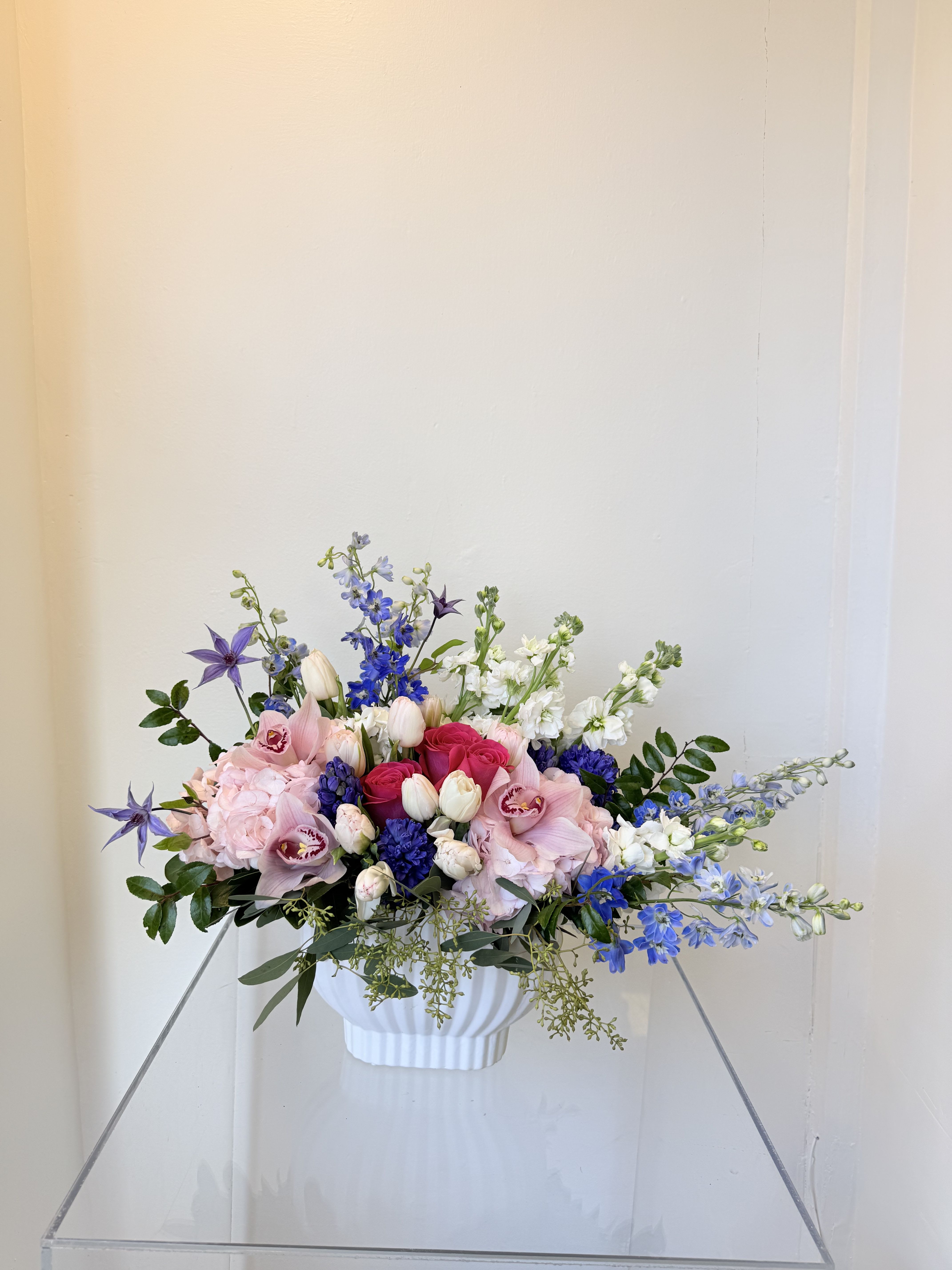 With love Mom  -   A delicate harmony of blush pinks, soft whites, and vibrant touches of blue, this design blends roses, tulips, orchids, and seasonal blooms in a lush garden-style arrangement. Light, airy, and full of movement, it’s a graceful expression of love and appreciation—perfect for celebrating Mom.