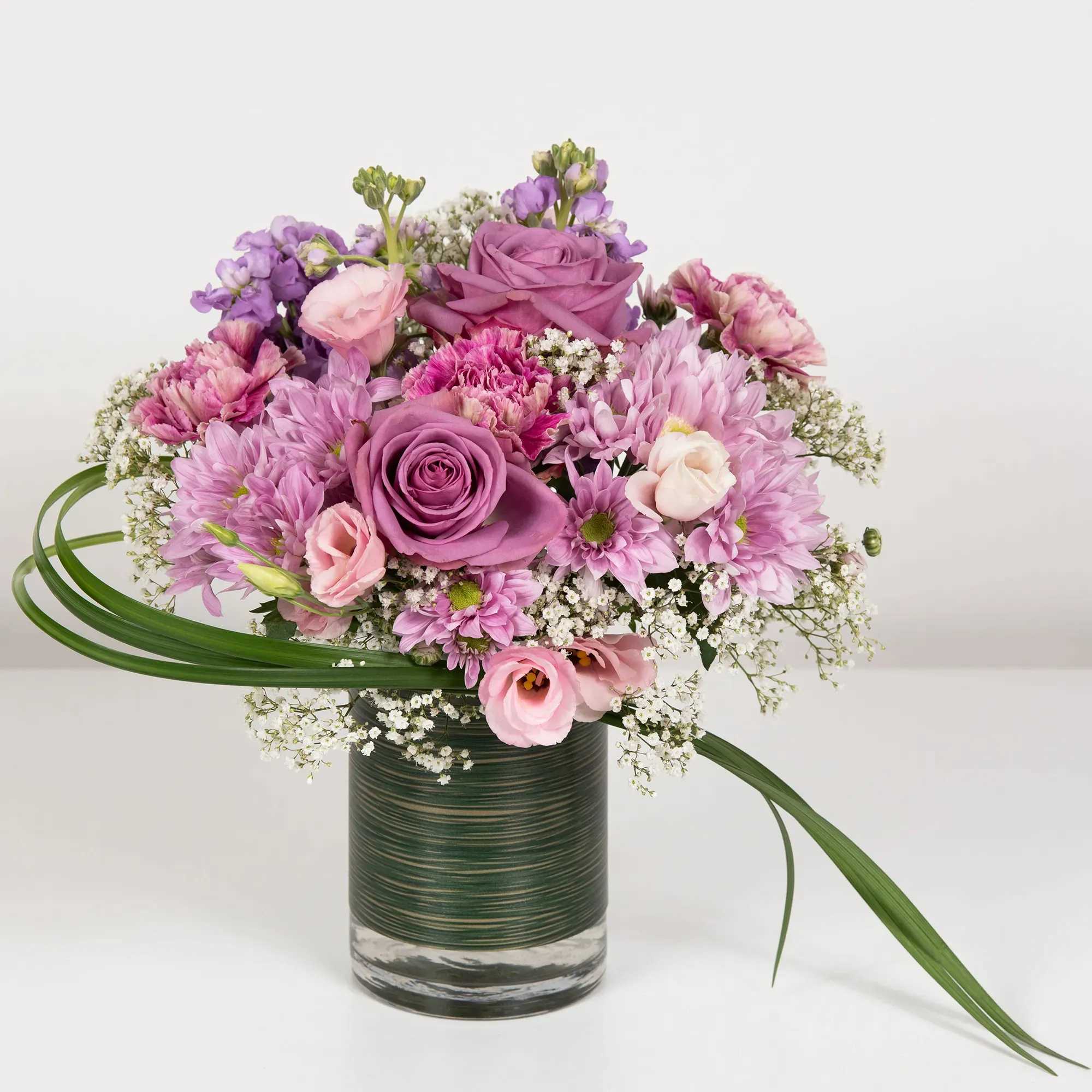Pink and purple mixed bouquet in a glass vase with long green leaves