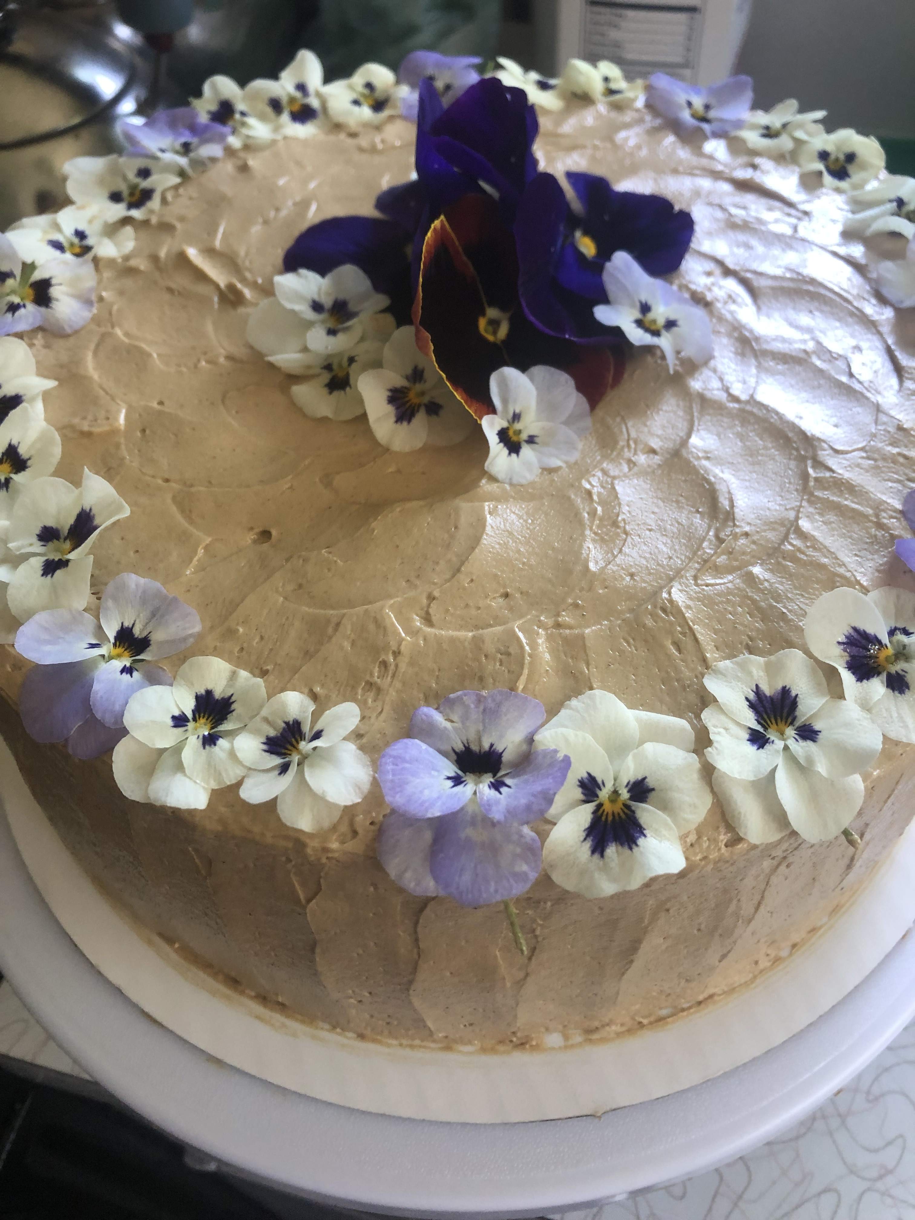Round frosted cake topped with purple and white edible flowers