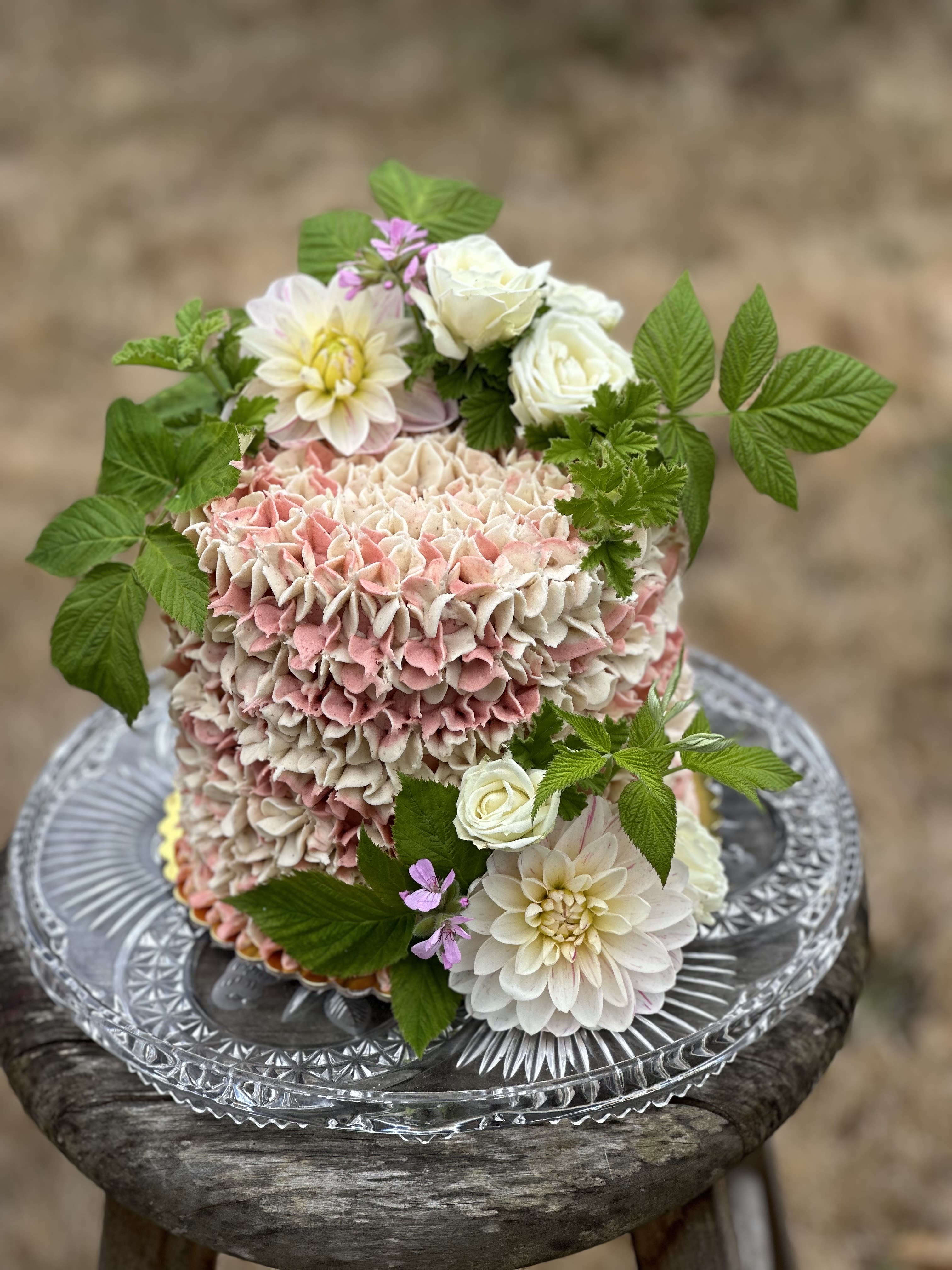 Pink and white floral cake with roses and dahlias on a glass stand