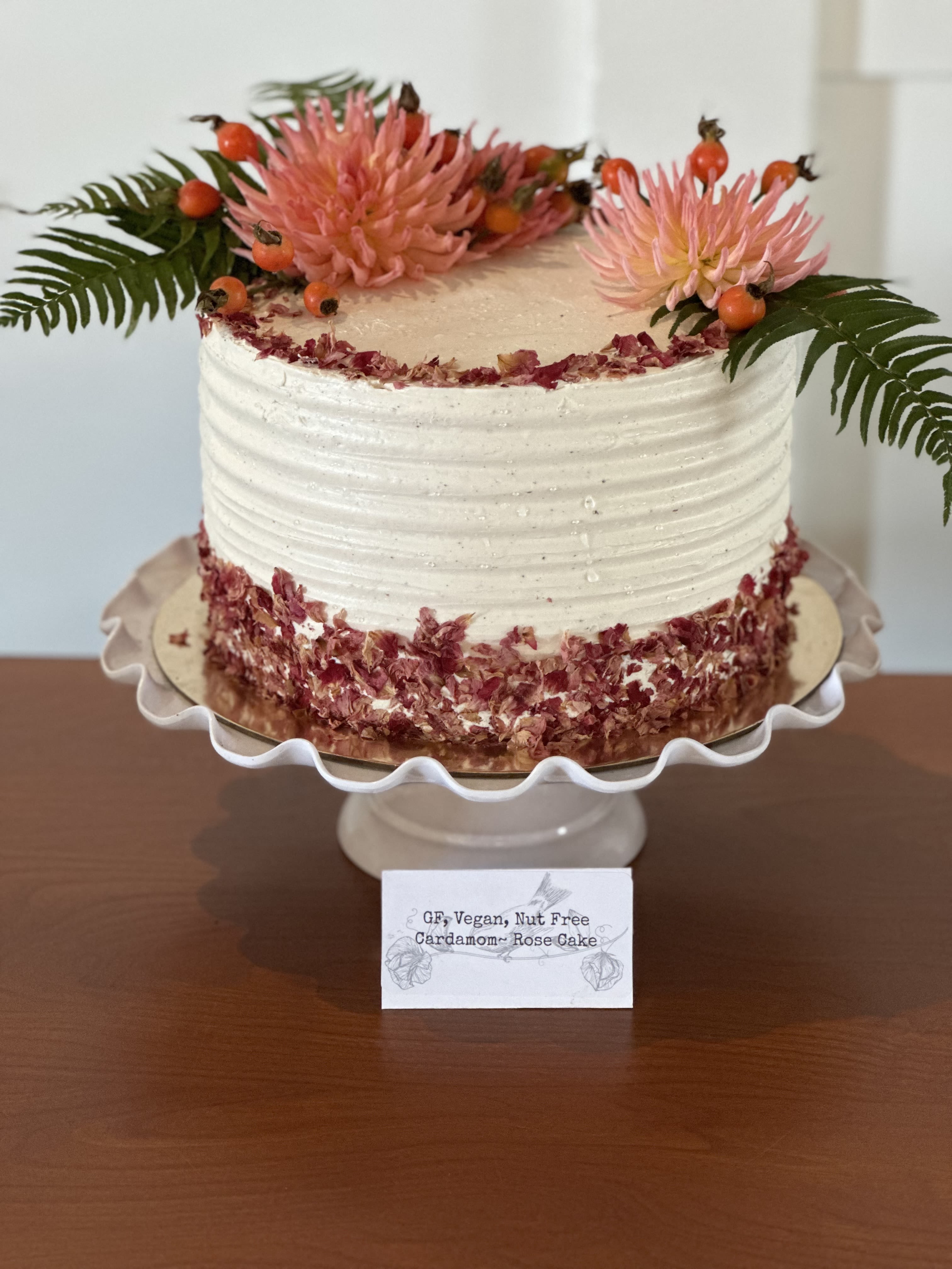 White frosted cake topped with pink flowers and fern fronds