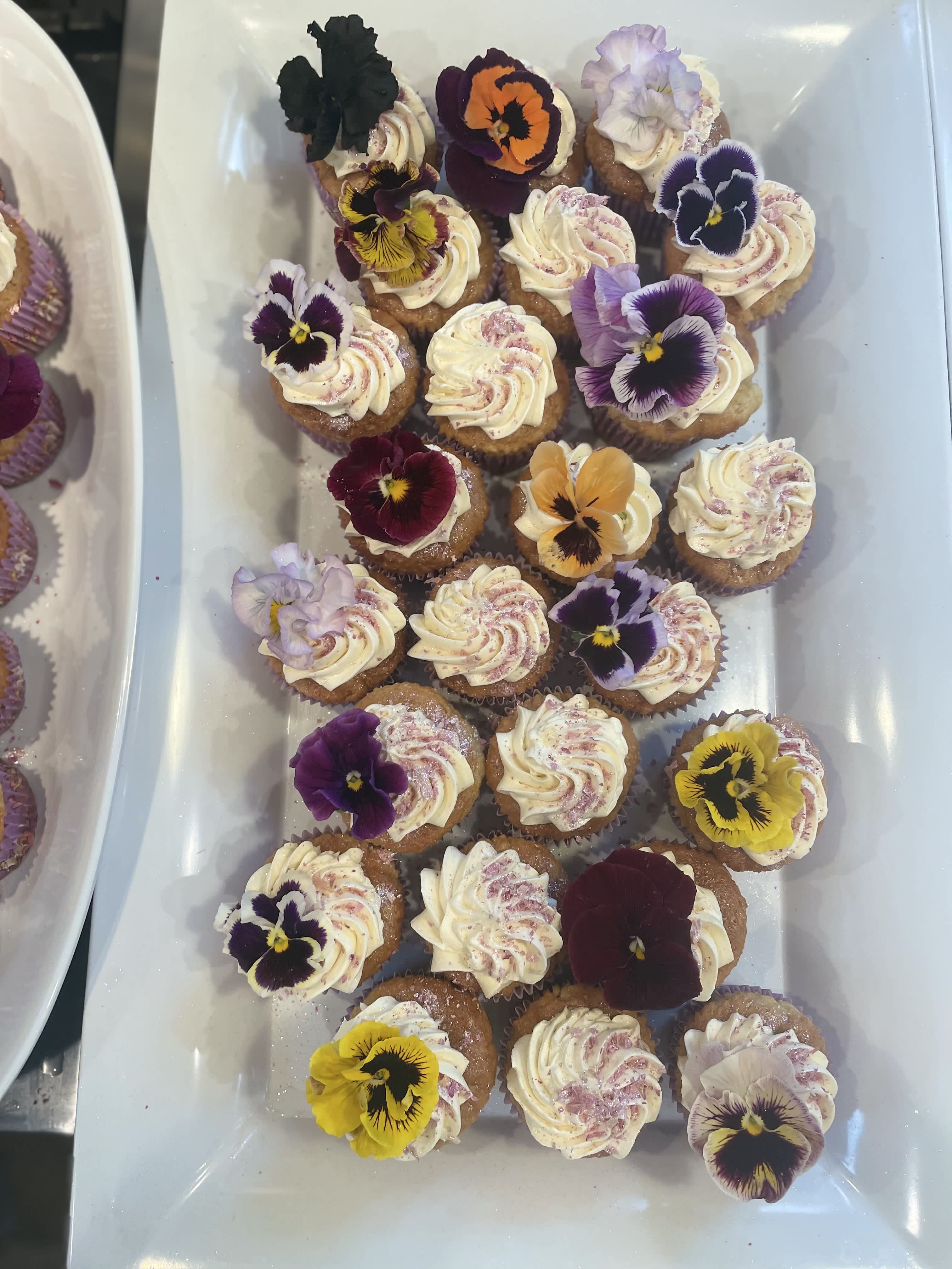 Tray of frosted cupcakes topped with colorful edible flowers