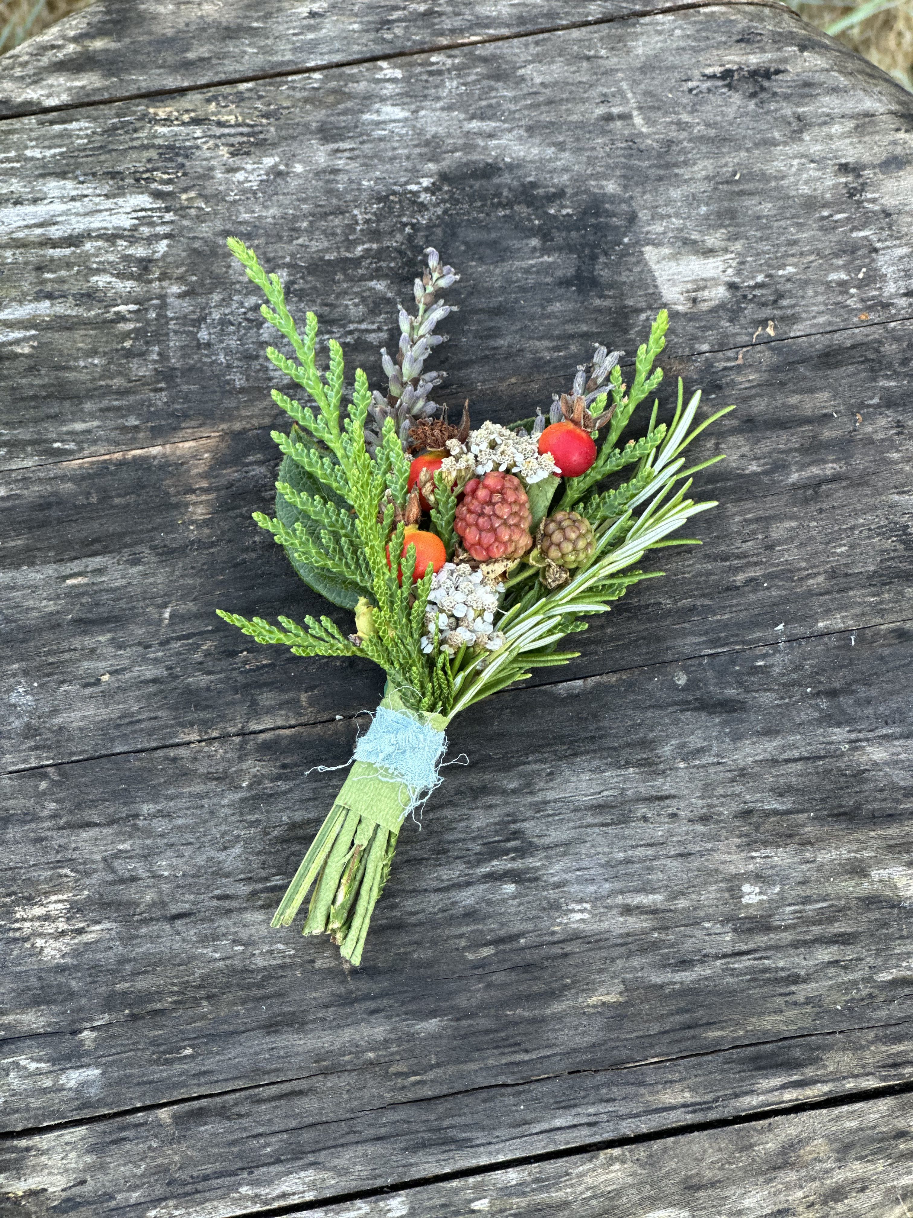 Small boutonniere with berries and greenery tied with blue ribbon