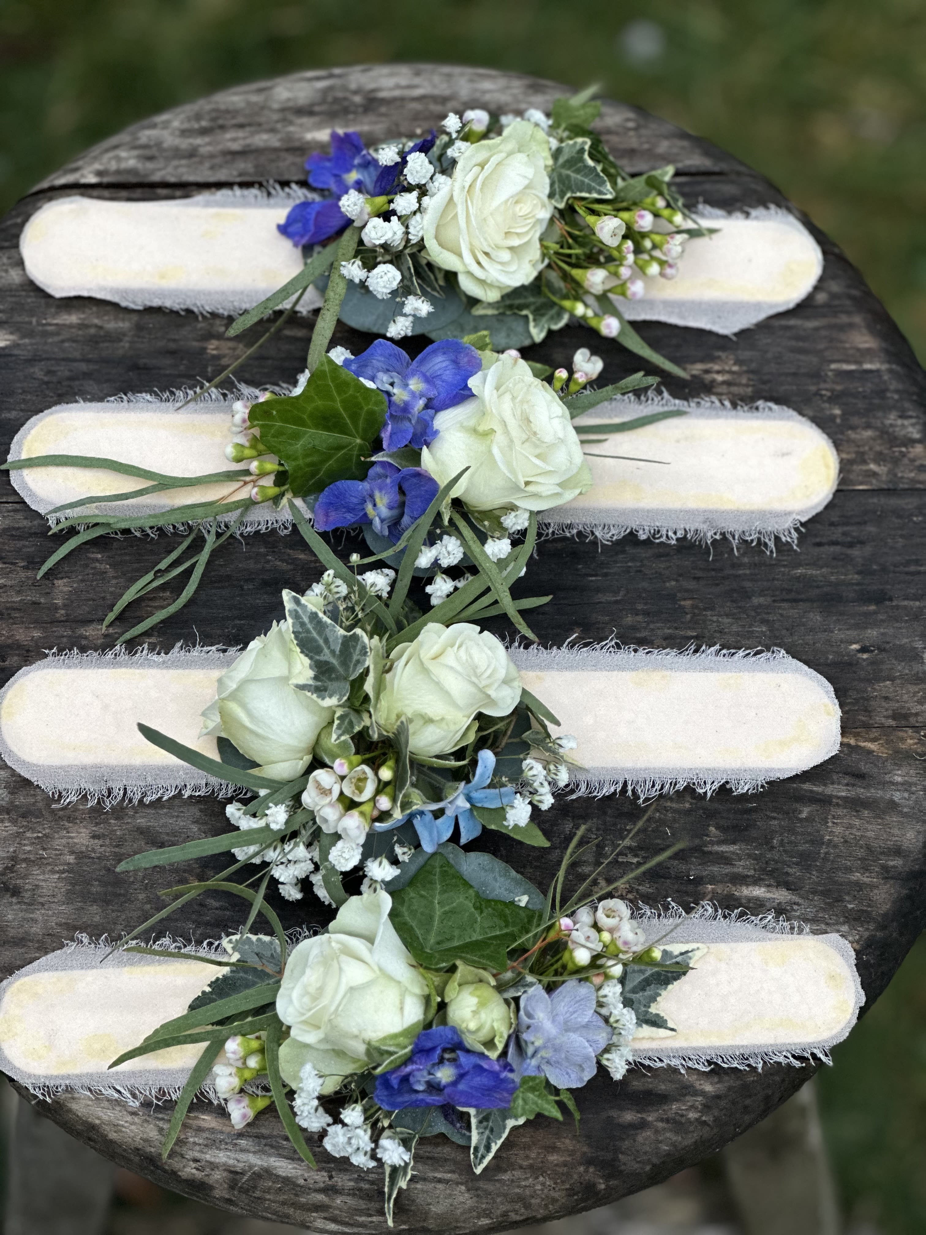 Four floral wrist corsages with white roses and blue flowers on pale bands
