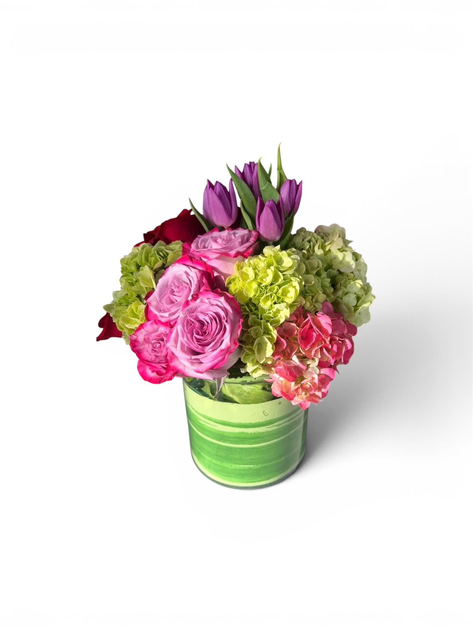 Mother’s Day! You are My World - A bright, playful mix of pink roses, purple tulips, and green-and-pink hydrangeas makes this flower arrangement a joyful everyday gift - perfect as a birthday bouquet, a thank-you surprise, or a just-because pick-me-up for someone who lights up a room. The combination of saturated pinks and purples set against a lime-green glass vase gives the design a lively, cheerful energy that reads as both modern and heartfelt; the person you're thinking of will feel genuinely seen and celebrated when these arrive.  The arrangement is rounded and compact with tulips extending slightly above the lower blooms to add graceful height and movement. You'll find soft pink roses, rich purple tulips, and clusters of green and blush hydrangea artfully arranged in a clear lime-green glass vase that enhances the color contrast. The composition is full without being fussy, offering lush texture from the hydrangeas and classic romance from the roses.  Ideal for birthdays, notes of appreciation, or simple gestures of affection, this bouquet suits recipients who love vibrant color and a touch of whimsy. Care is simple: keep water fresh, trim stems every few days, and display away from direct heat or drafts to prolong bloom life.
