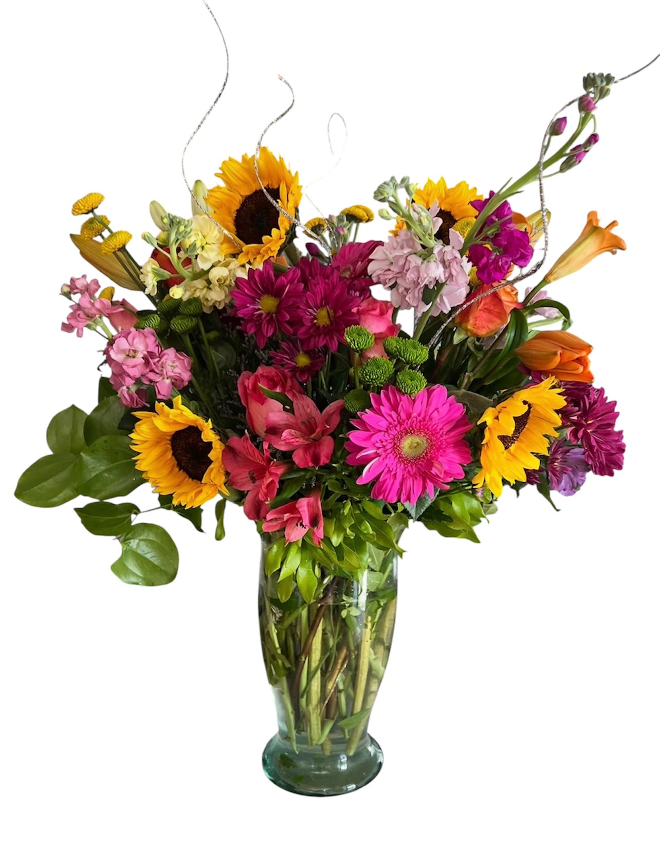 Mother’s Day Impress Them! - Bright sunflowers and hot pink gerbera daisies make a bold first impression in this mixed-color bouquet-perfect as a birthday bouquet, congratulations arrangement, or an everyday gift to lift someone's spirits. The vibrant mix of pink, yellow, and orange reads joyful and celebratory, the kind of bouquet that makes the person you're thinking of feel noticed and genuinely cheered.  This full, asymmetrical arrangement combines sunflowers, gerbera daisies, alstroemeria, lilies, and chrysanthemums set in a clear glass vase. Tall stems and curling decorative accents rise above a dense cluster of blooms, giving texture and movement while the saturated palette keeps the look fresh and energetic. The clear vase showcases stems for a clean, modern presentation and fits well on tabletops or entryway consoles.  Ideal for sending to a friend, colleague, or family member to mark a happy milestone or simply brighten their day, this bouquet arrives ready to display. To prolong bloom life, keep in a cool spot out of direct sunlight, refresh the water every other day, and trim stems at an angle before placing them back in the vase.