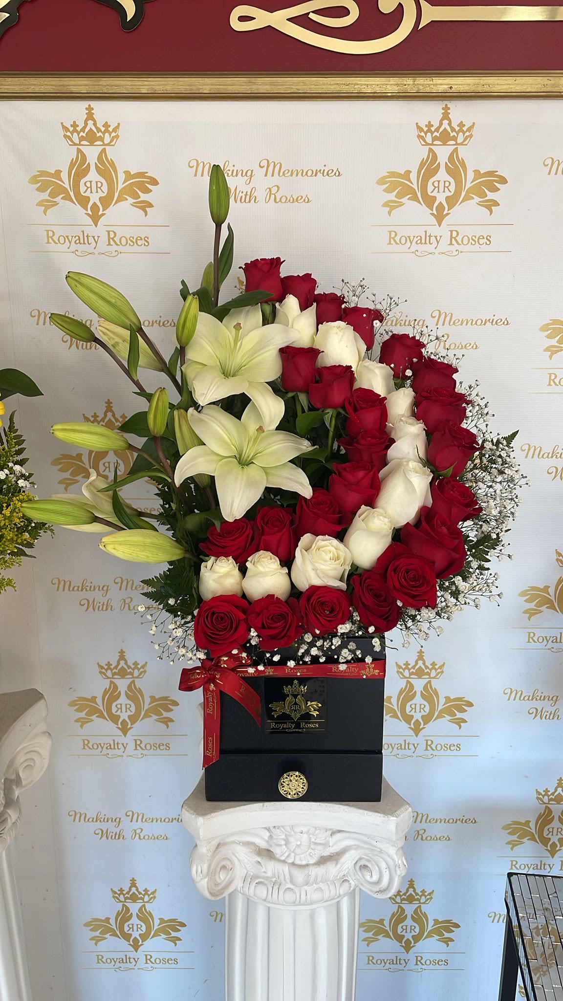 Half Moon Bicolor  - A dramatic red-and-white bouquet arranged in a sleek black gift box-this Half Moon Bicolor arrangement brings classic romance with modern polish. Perfect as Mother's Day gift or an anniversary roses gift or a gesture of love and sympathy, the tight band of red and white roses paired with open white lilies creates a striking contrast that reads both formal and heartfelt; the tall, rounded silhouette makes a strong visual statement the person you're thinking of will notice from across the room.  Tightly packed red and white roses form the core, accented by open white lilies and several unopened lily buds for texture and gentle fragrance. The flowers rise from a matte black presentation box finished with a red ribbon and decorative bow, giving the arrangement a refined, ready-to-give look. Sized to command attention on a side table or mantel, it arrives arranged and gift-ready so your recipient feels truly seen and celebrated.