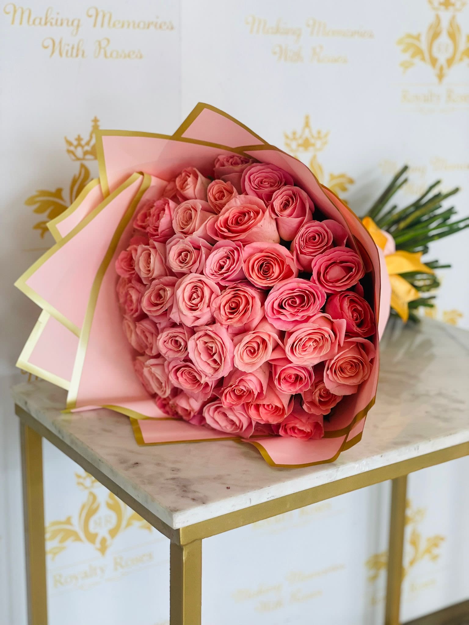 Pink Pastel Bouquet - A lush cluster of pink roses arranged in a rounded, hand-tied form-this Pink Pastel Bouquet is designed to make the person you're thinking of feel lovingly celebrated. Perfect for an anniversary, birthday, or Mother's Day, the tightly layered blooms create a soft, romantic visual that reads feminine and refined the moment it's opened.  Each medium-sized bouquet features densely packed pink roses with touches of white in the overall palette, wrapped in soft pink decorative paper edged with gold and finished with a ribbon for a polished presentation. Because it's arranged as a hand-tied gift bouquet rather than a vase display, it's ideal for handing to someone at the door or carrying into a celebration-she'll feel truly seen the instant she receives it.