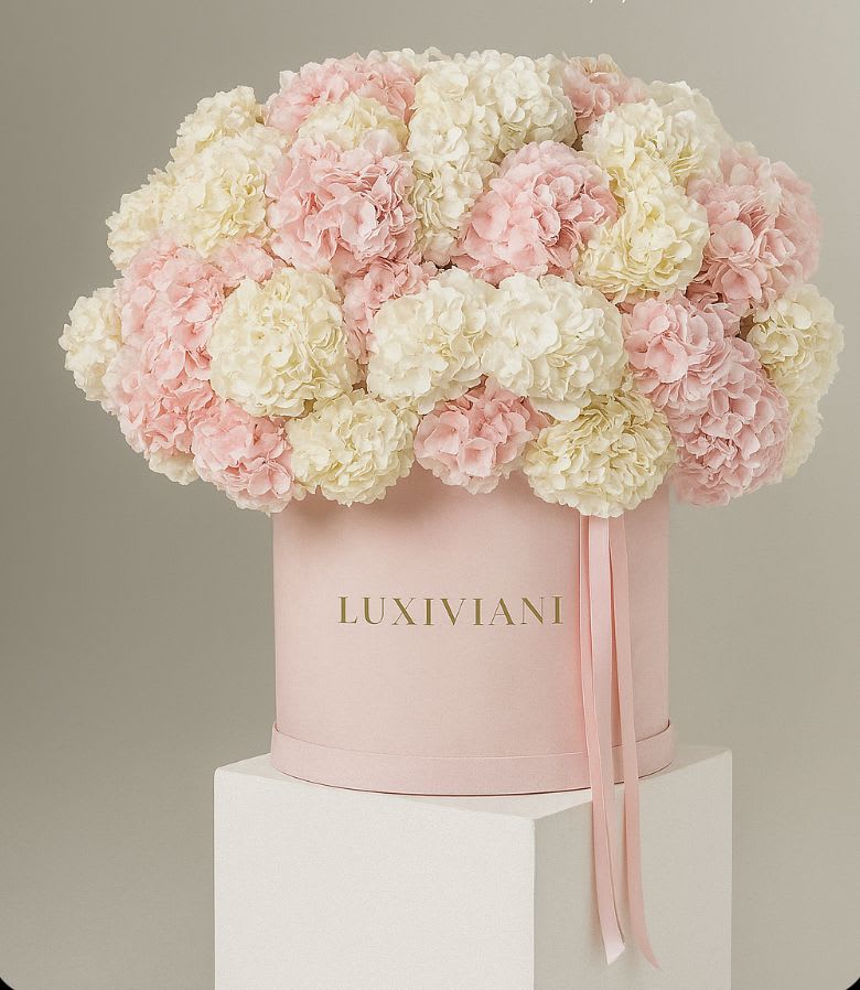 Pink and white hydrangeas arranged in a round hatbox with ribbon