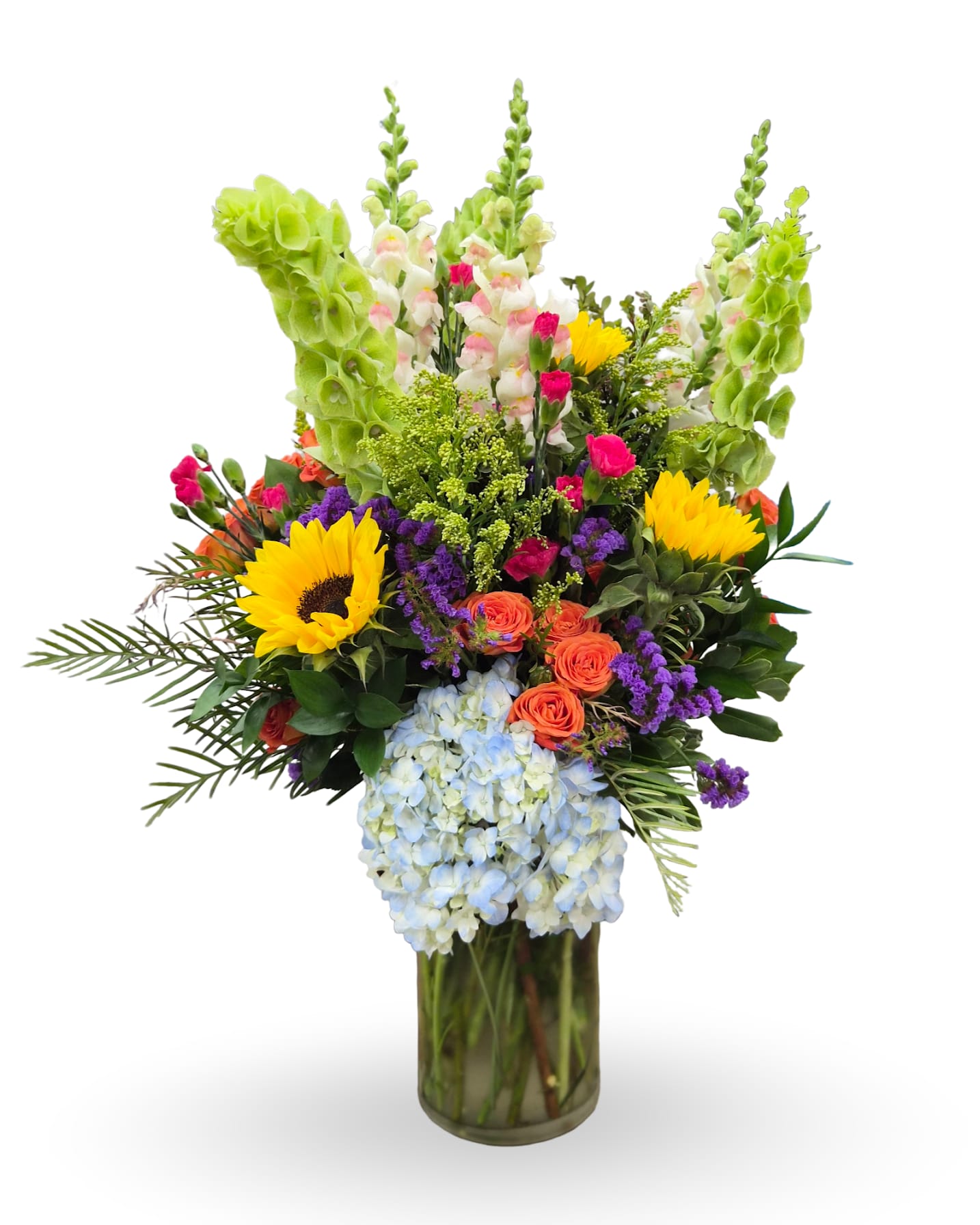 Spring Happiness - Lime-green snapdragon spikes and bright yellow mini sunflowers give this Spring Happiness flower arrangement an uplifting, sunlit presence-perfect as a birthday bouquet, anniversary surprise, or a cheerful Mother's Day gift. The tall vertical lines set against a dense, rounded center create a joyful, slightly tropical look that makes the person you're thinking of feel celebrated, seen, and energized whether you're saying "thank you," "congratulations," or "get well soon."  This mixed-color arrangement features blue hydrangea, orange spray roses, hot pink mini carnations, light pink snapdragons, purple statice, solidago, and bells of Ireland artfully layered with gerbera-style accents for a full, textured composition. The vivid palette of purple, orange, green, yellow, blue, and mixed tones reads bright and festive; everything arrives arranged in a clear glass vase that highlights the stems and keeps the design looking fresh on day one.  Ideal for spring and summer occasions-from retirements and Grandparent's Day to Boss's Day or Admin Professionals' Week-this bouquet brings instant warmth to a hospital room, office desk, or dining table. For best longevity, keep the vase filled with fresh water and trim stems every few days; send a note at checkout to personalize this lively, feel-good gift.