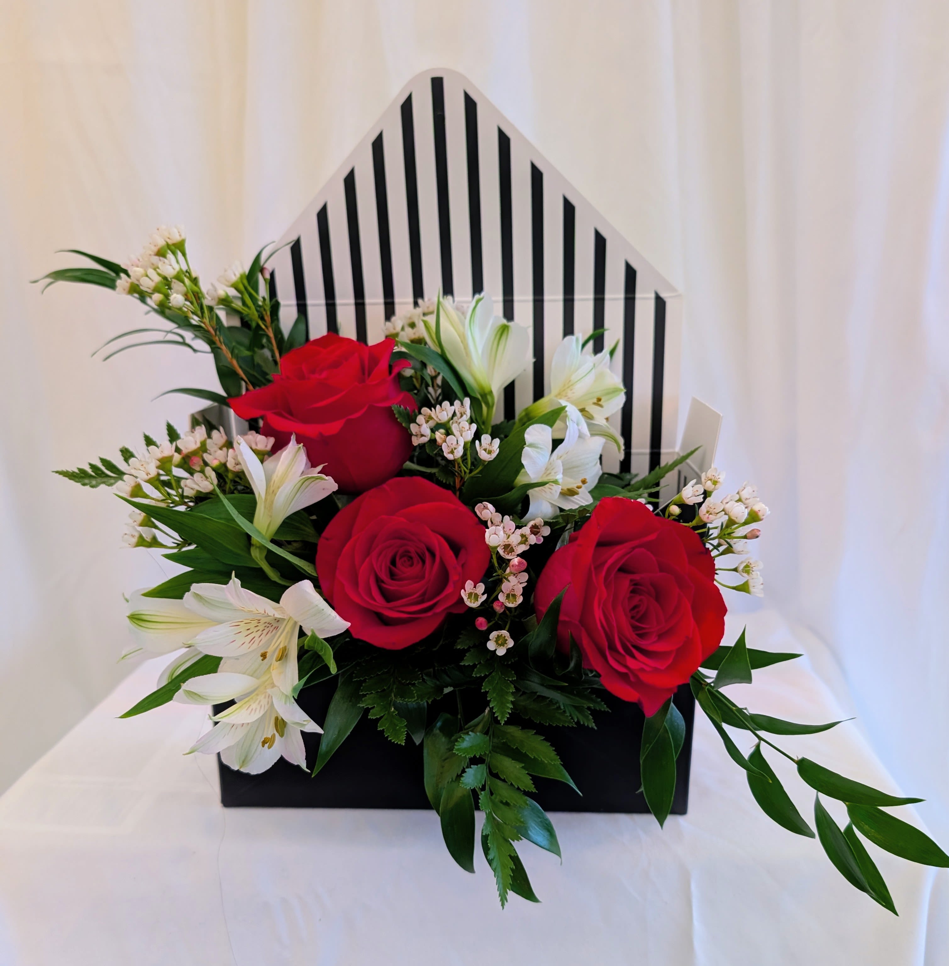 Red roses and white lilies arranged in a black box with a striped back panel.