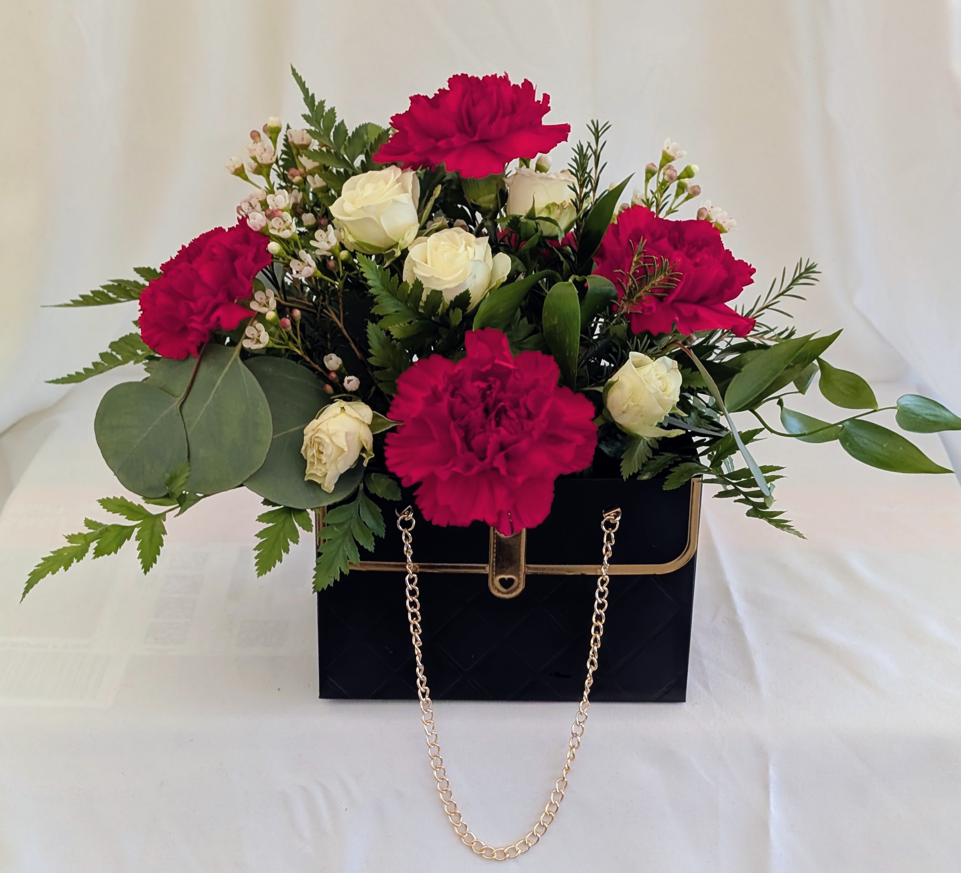 Pink carnations and white roses in a black handbag-style box