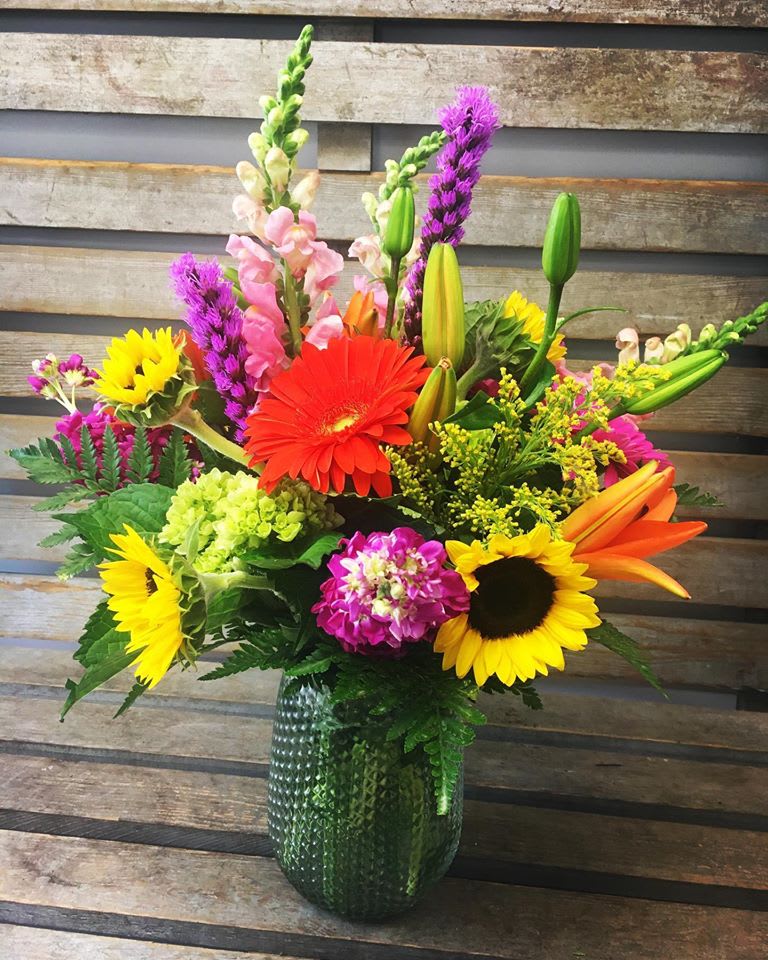 Colorful mixed bouquet in a green glass vase with sunflowers and lilies