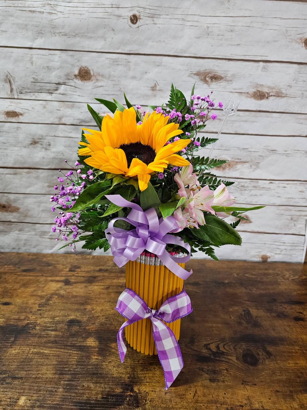 Sunflower bouquet in a pencil vase with purple ribbon and pink accent flowers