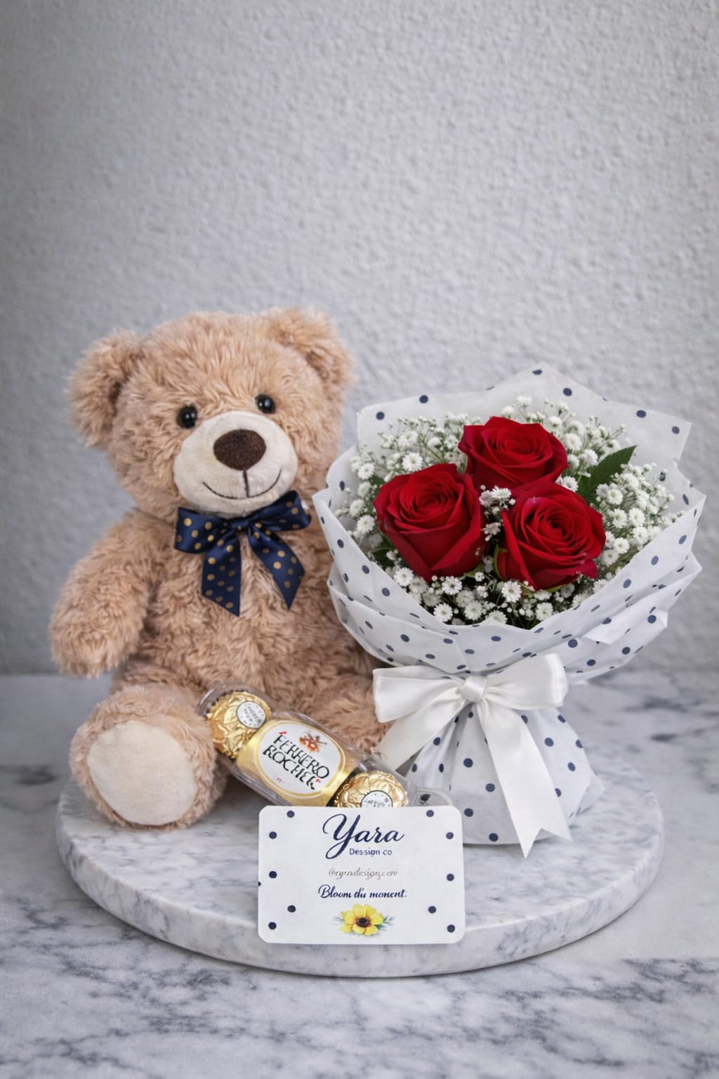 Sweet Bloom Bear - Three red roses tucked into a compact bouquet make an immediate, romantic impression-perfect as a birthday bouquet, anniversary surprise, or Valentine's Day gift. The Sweet Bloom Bear pairs those roses and delicate white filler flowers with a plush teddy bear and chocolate candies, so the person you're thinking of feels both cherished and celebrated the moment the box is opened.  The bouquet is wrapped in white paper printed with navy polka dots and finished with a white satin ribbon for a neat, joyful presentation; colors here are red, white, pink accents, and a touch of black in the pattern. Alongside the roses you'll find soft filler blooms that add texture and brightness, plus a gift card for your personal message. The set arrives ready to give-no extra wrapping needed-making it an easy, thoughtful choice when you want someone to feel truly seen.